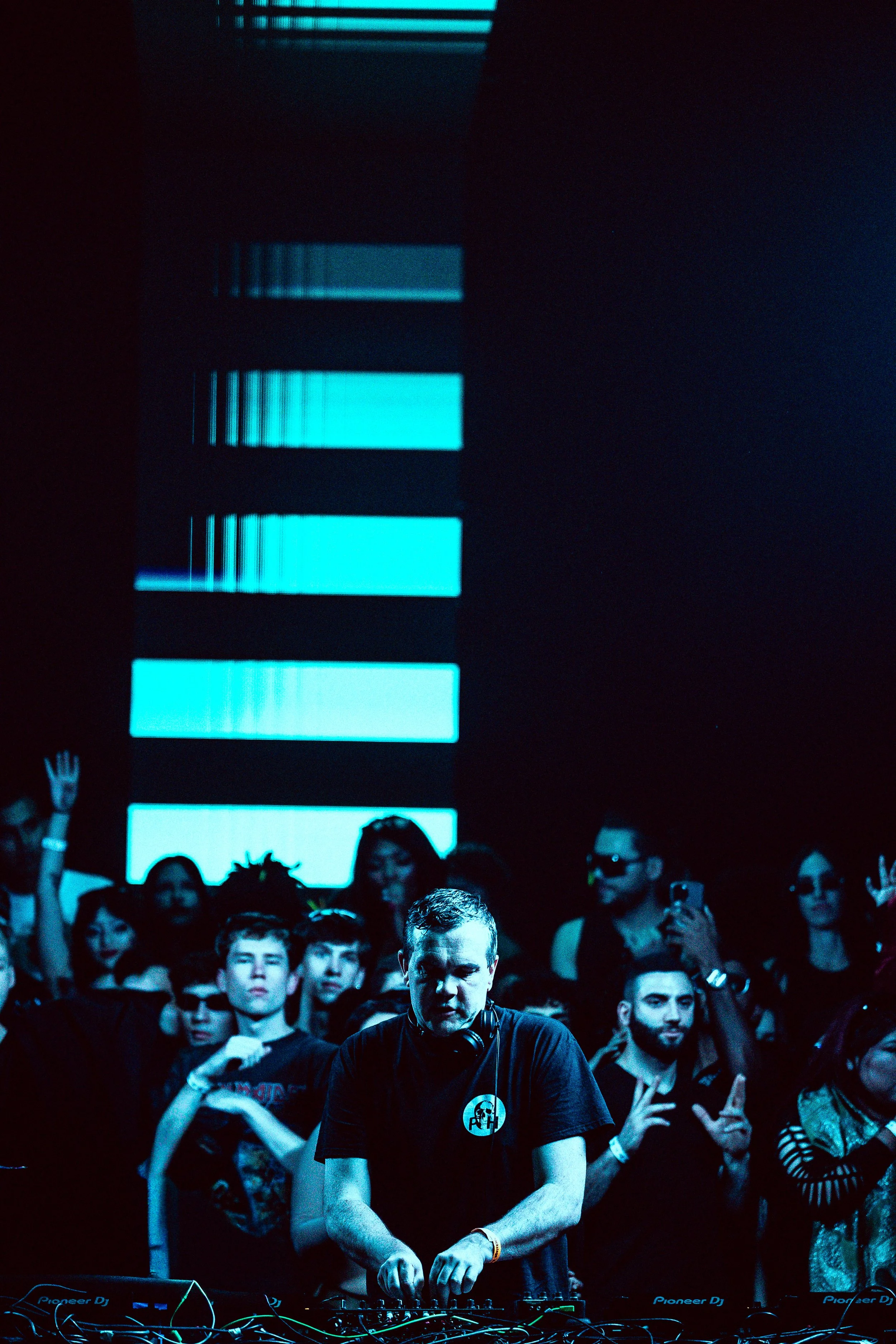 DJ performing at a crowded music event with a blue light display in the background.