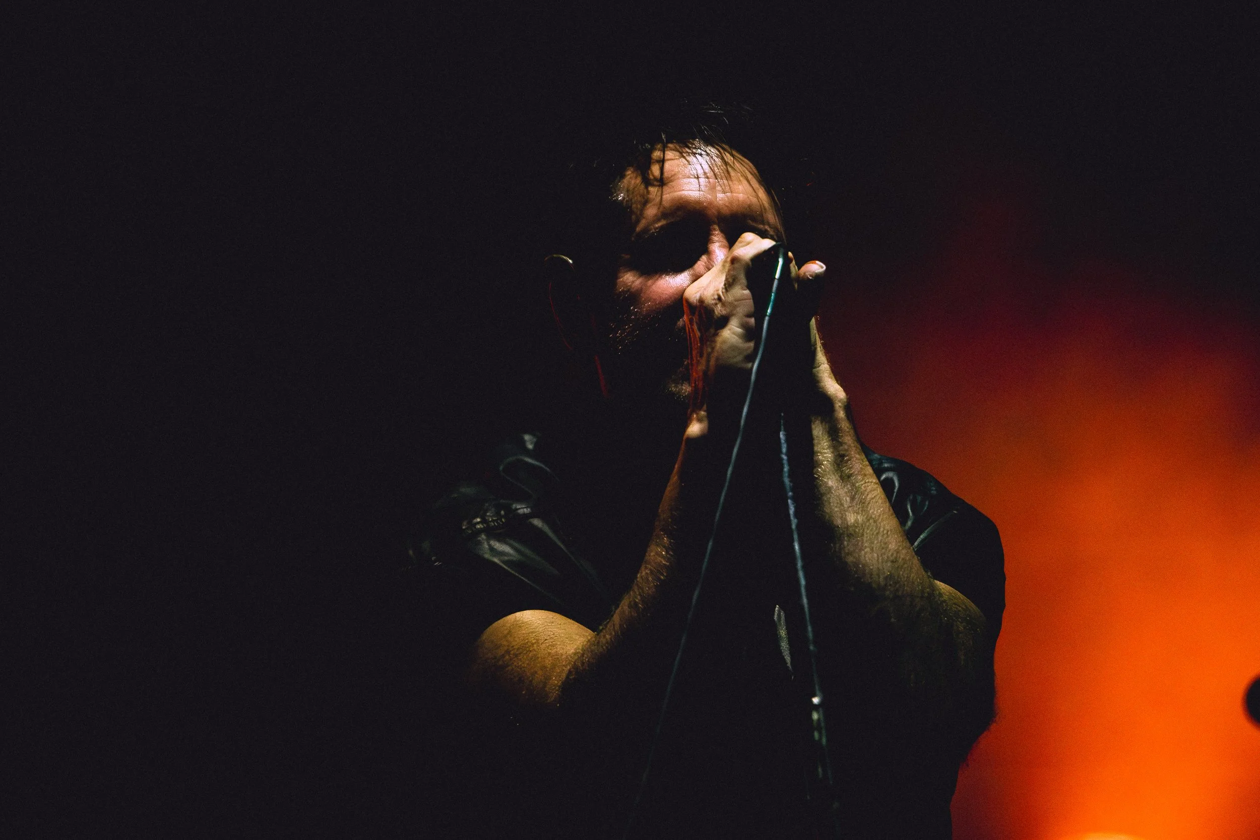 A man singing passionately into a microphone with a dark background and orange lighting.