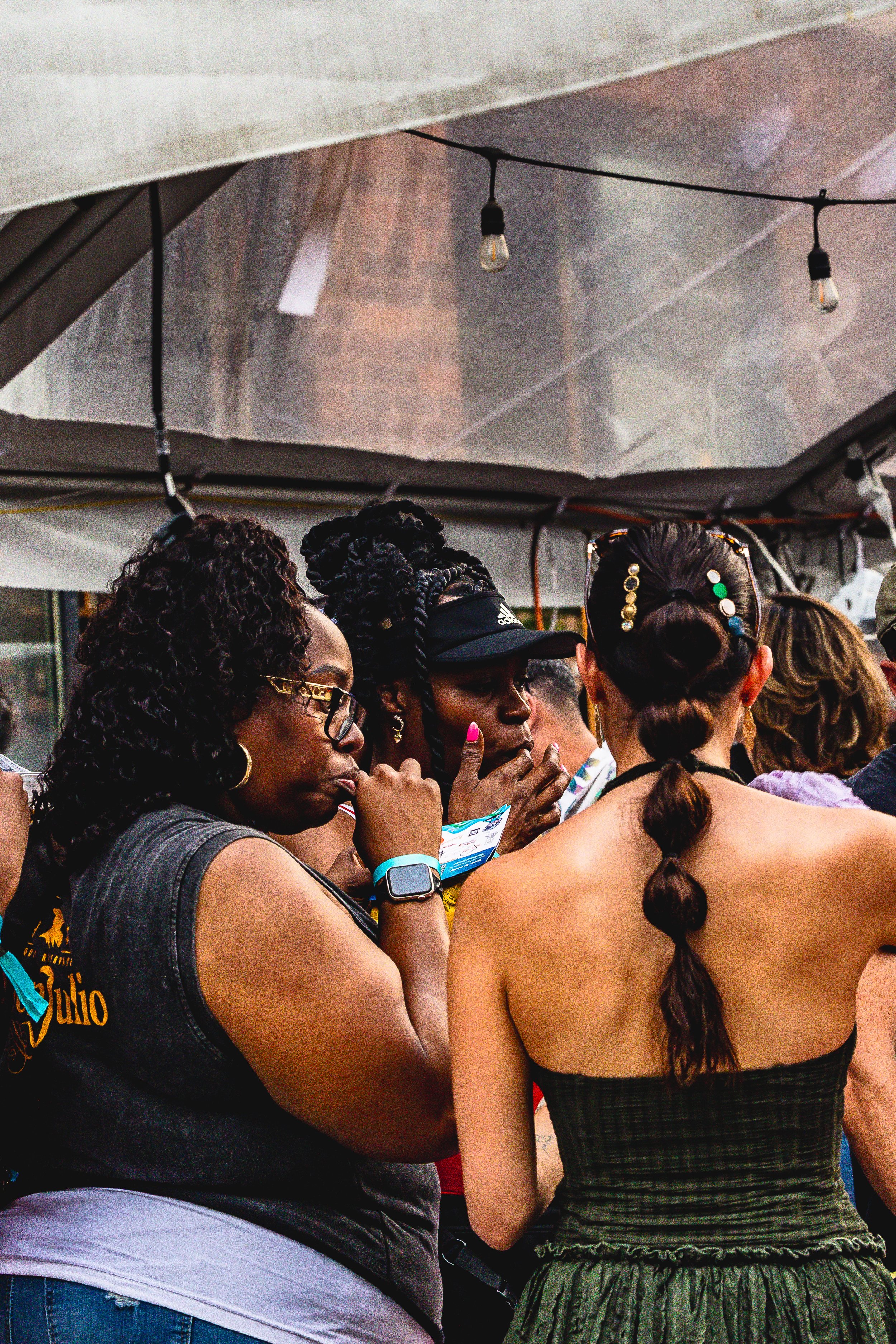 Group of women at an outdoor event under a canopy, engaging in conversation and looking attentive.