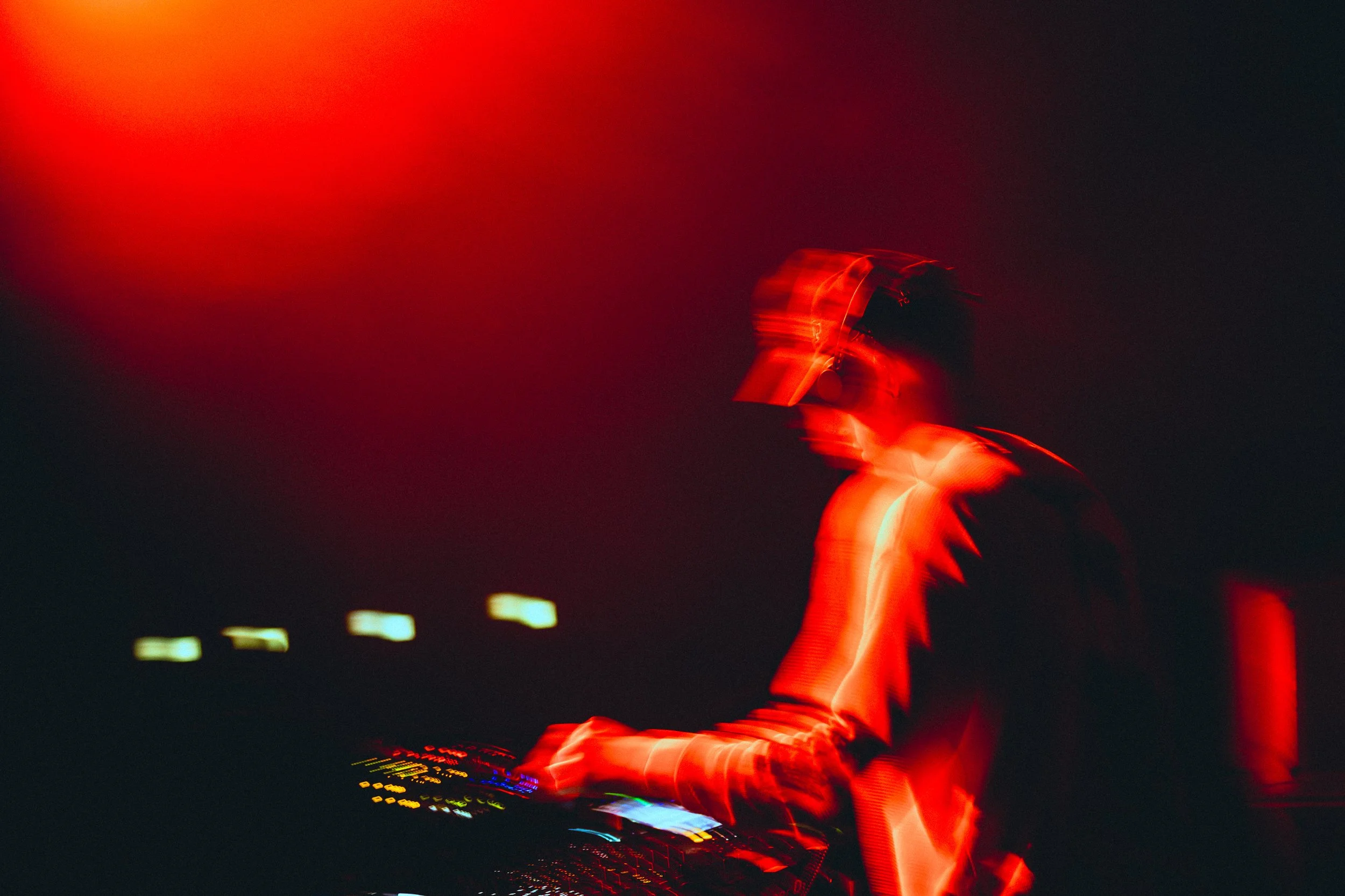 Cloonee wearing headphones at a turntable, illuminated by red and yellow lights in a dark setting, with motion blur effects.