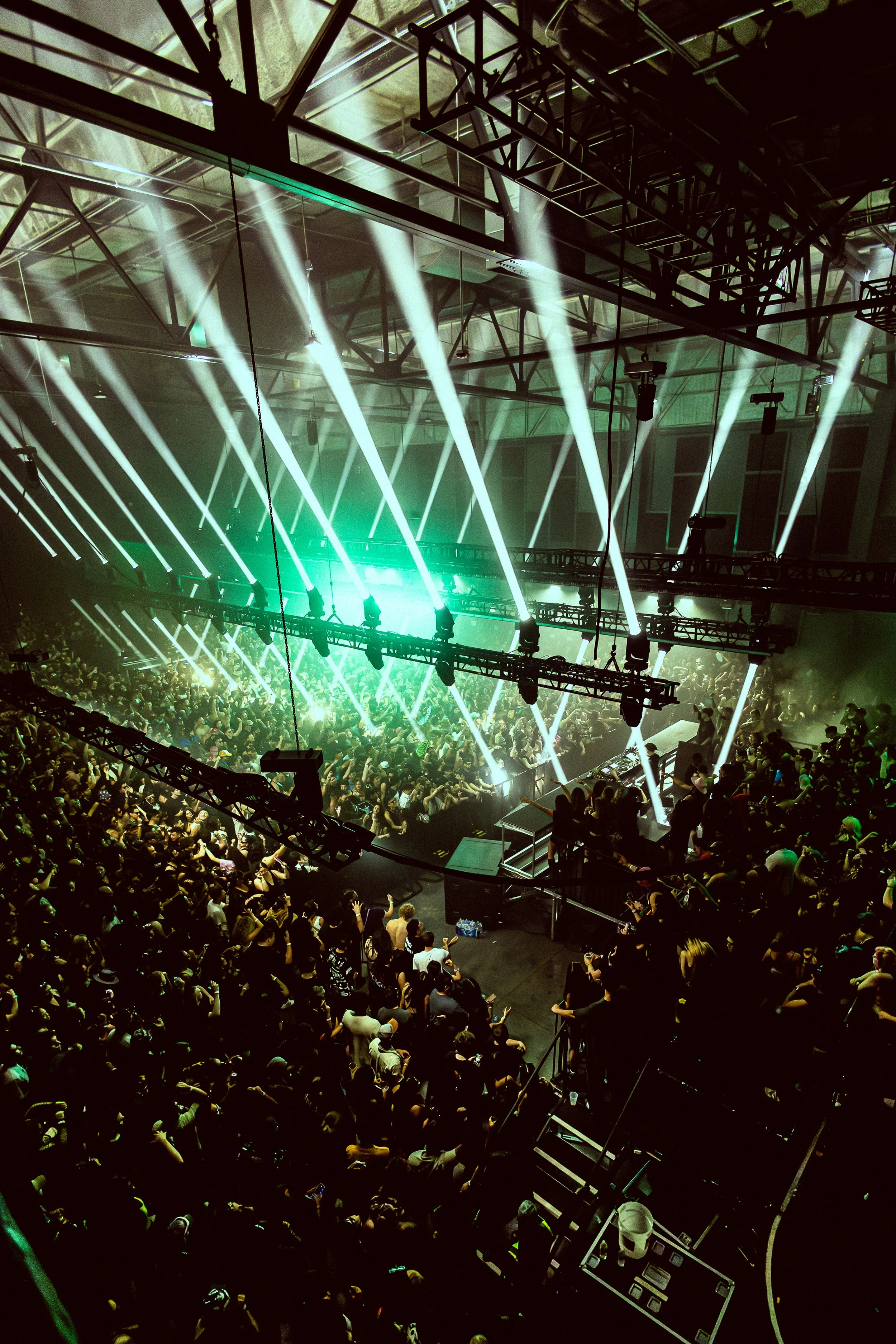 Crowd attending a concert or music event in a large indoor venue with bright stage lights and fog effects.