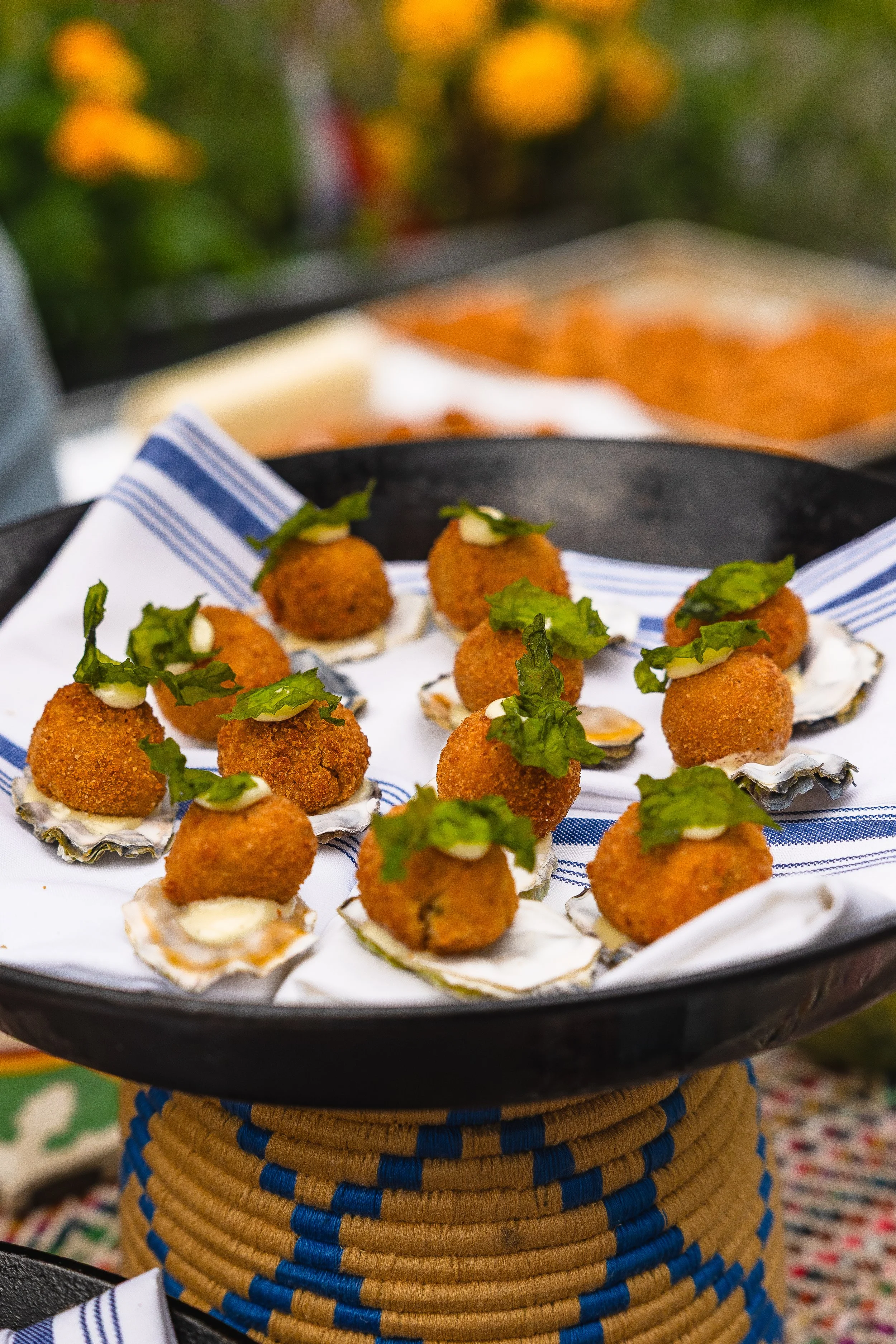 Fried oyster appetizers topped with leafy greens and a dollop of sauce, served on a black tray lined with a white napkin with blue stripes.