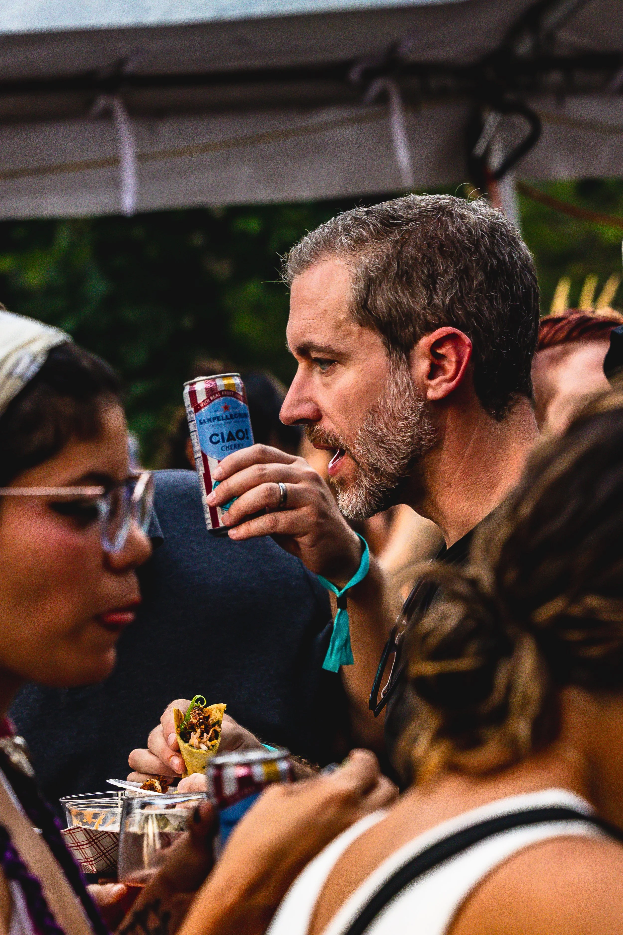 People at an outdoor gathering, with one man drinking from a can and others holding food and drinks.