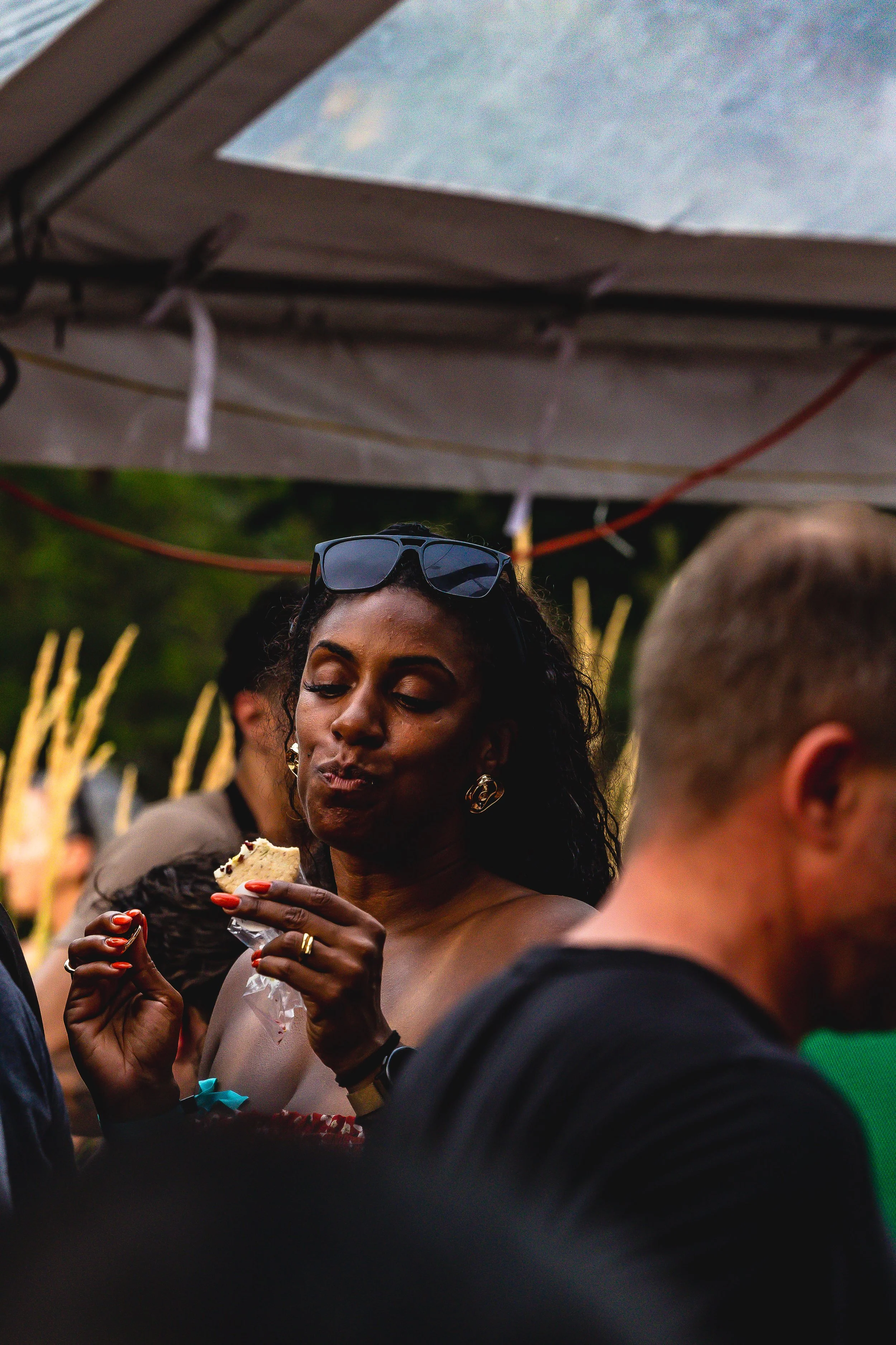 A woman with sunglasses on her head enjoying a snack at an outdoor event.