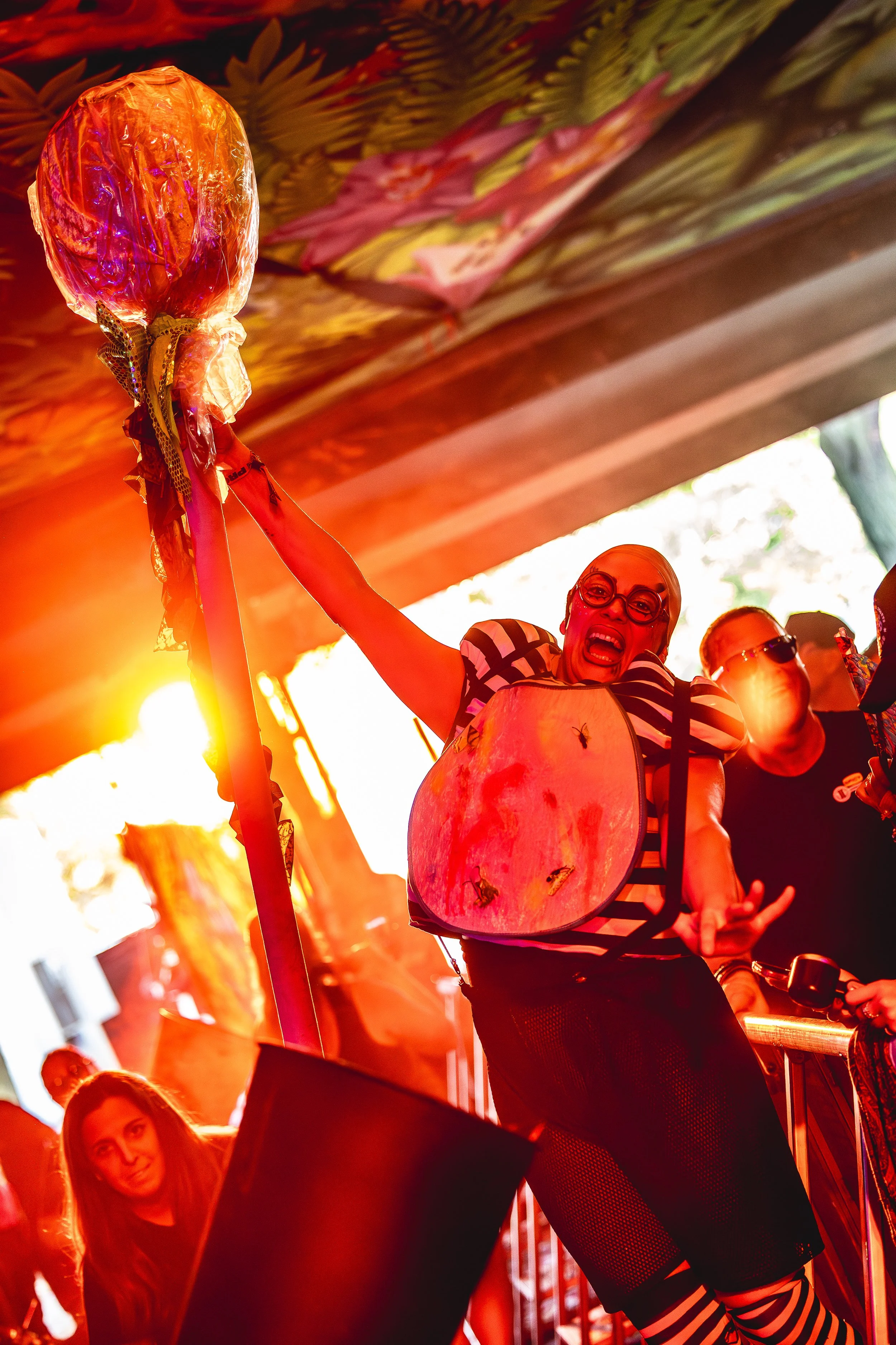 A woman enthusiastically holding a stick with a bat-shaped object wrapped in colorful plastic under a decorated ceiling during a lively event or festival.