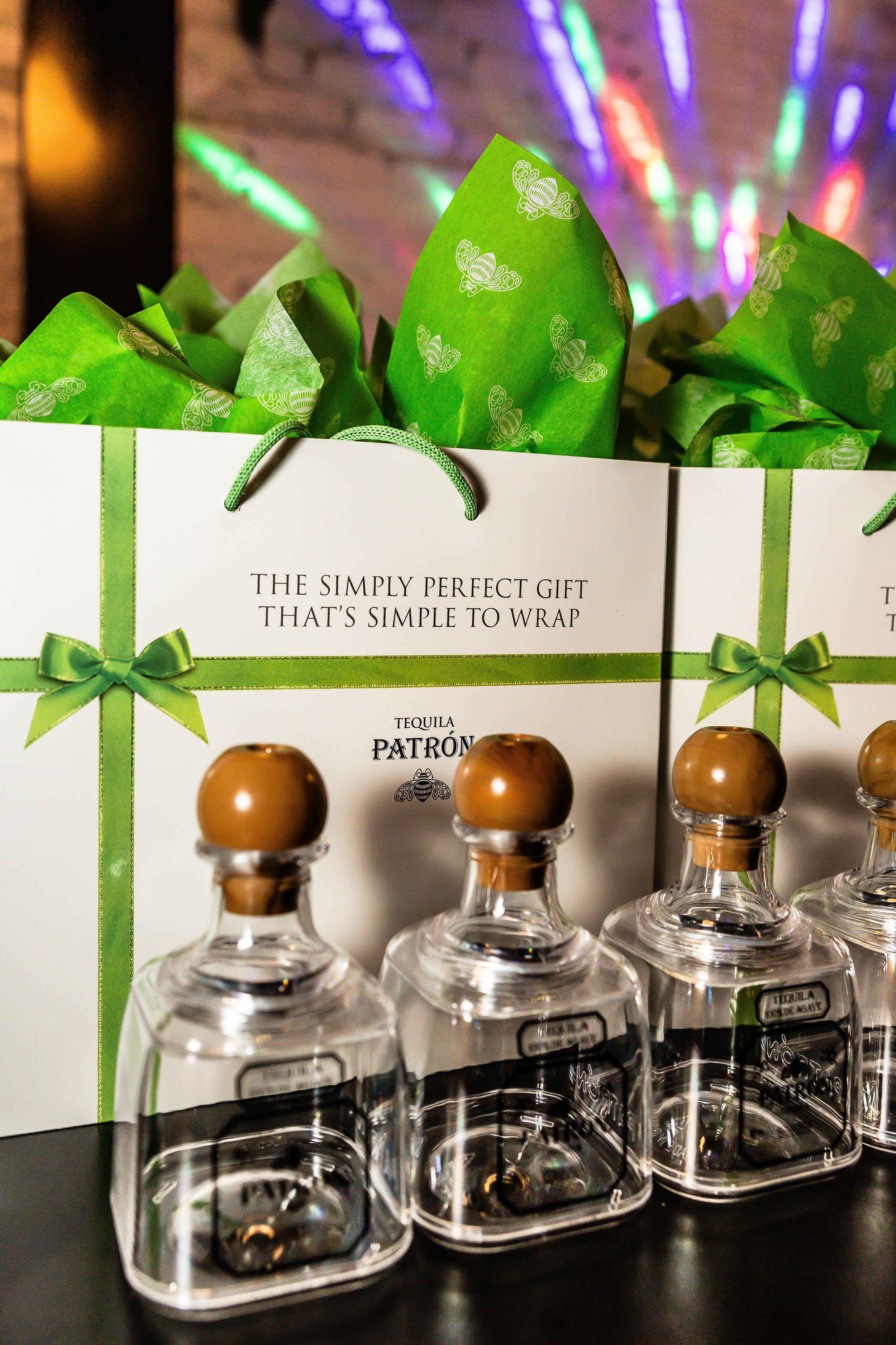 A display of Tequila bottles in front of a gift bag with green wrapping paper inside. The bag has a message about being a simple, perfect gift to wrap.