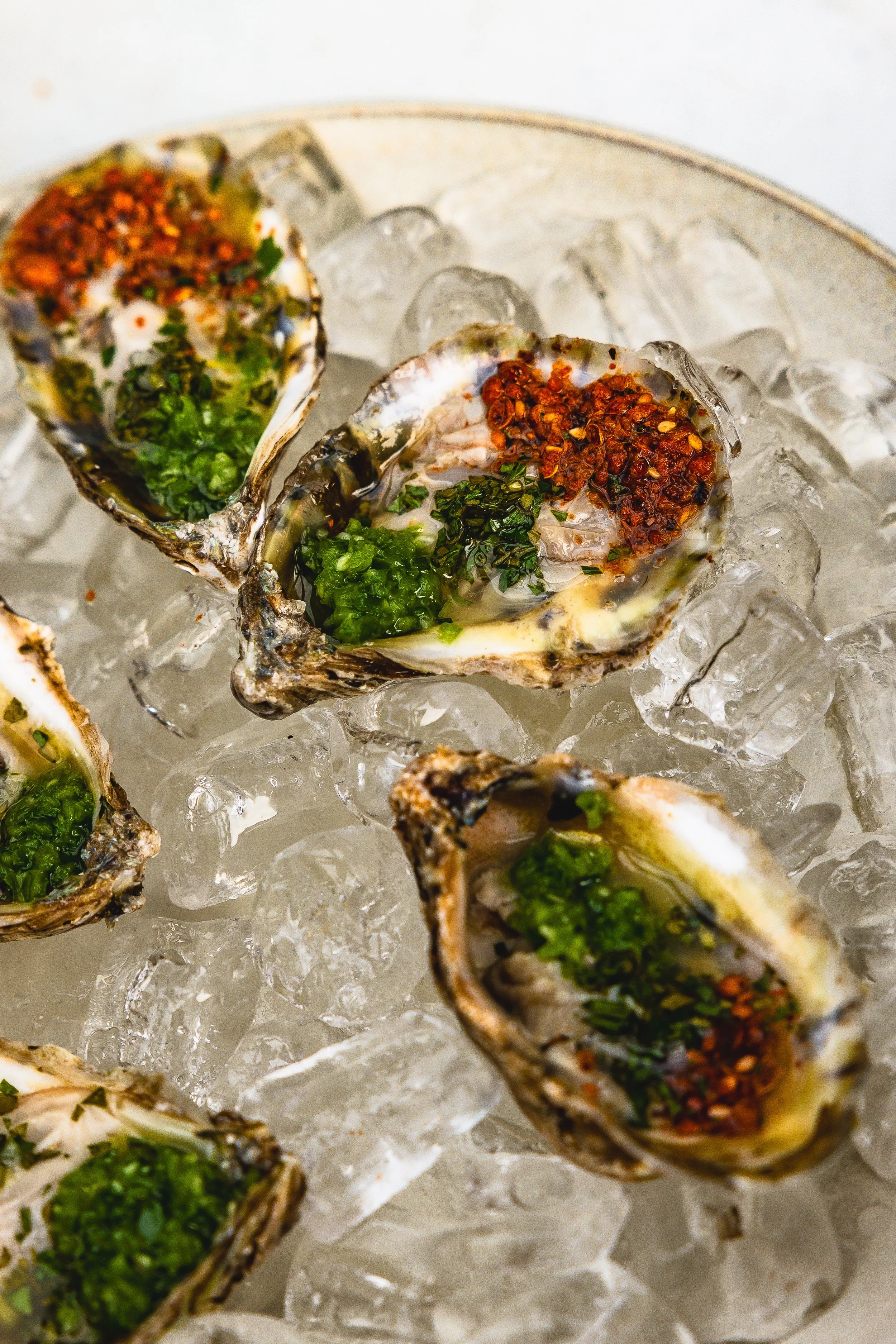 Oysters on ice garnished with chopped herbs and red pepper flakes.