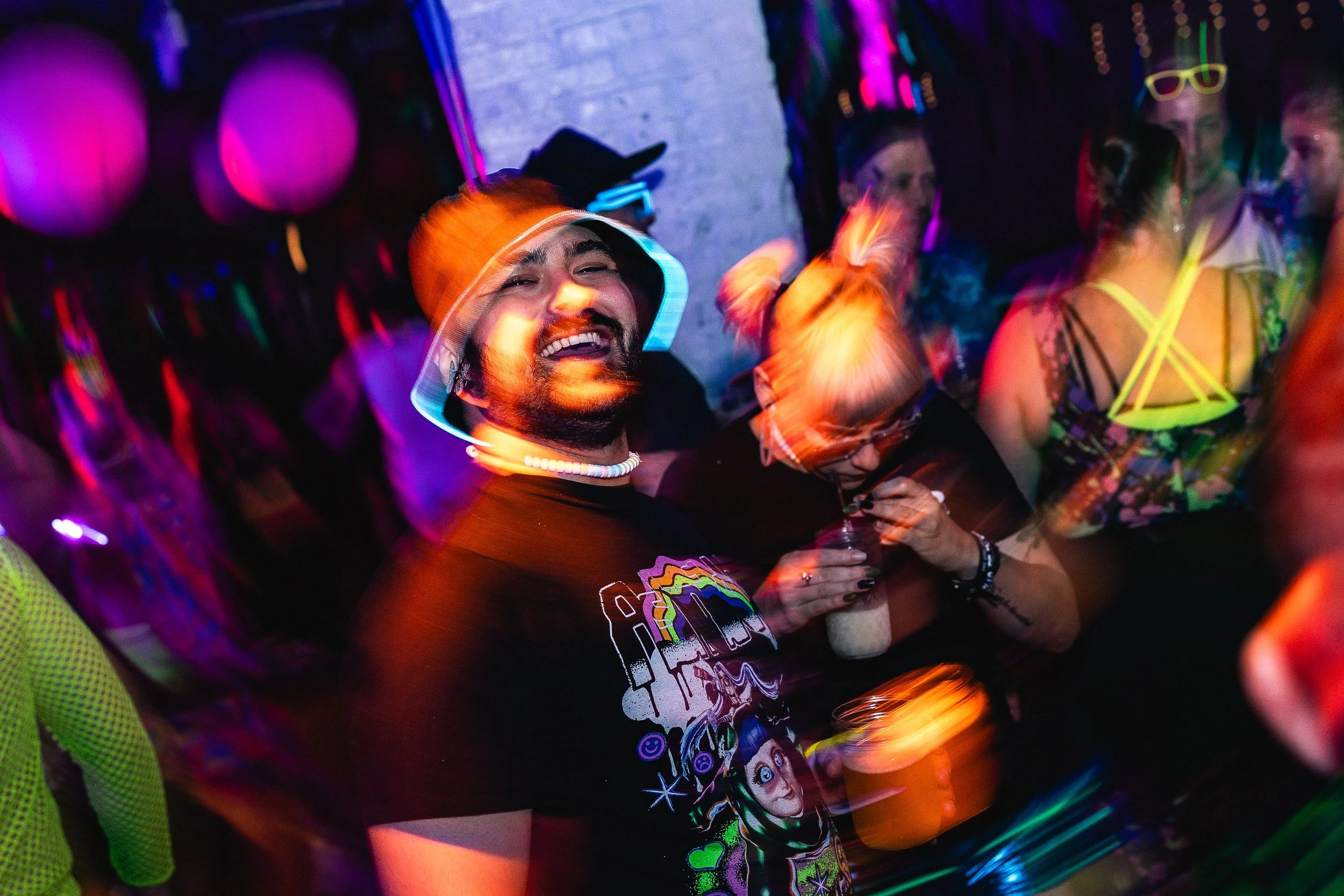 People enjoying a party with neon and glow-in-the-dark accessories, dancing and drinking under vibrant lighting.