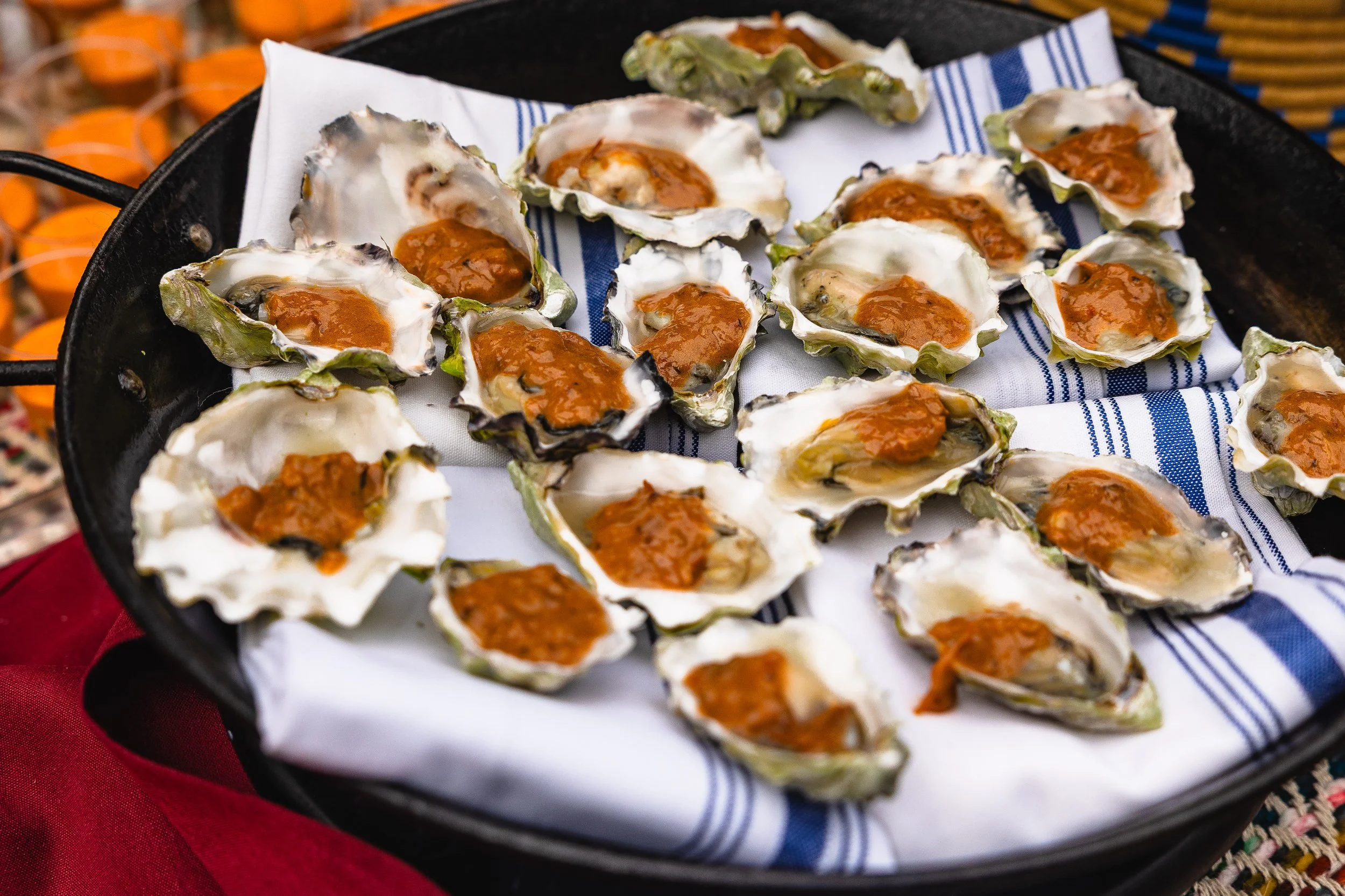 Oysters on the half shell with orange sauce, served on a bed of white and blue striped cloth in a black serving tray.