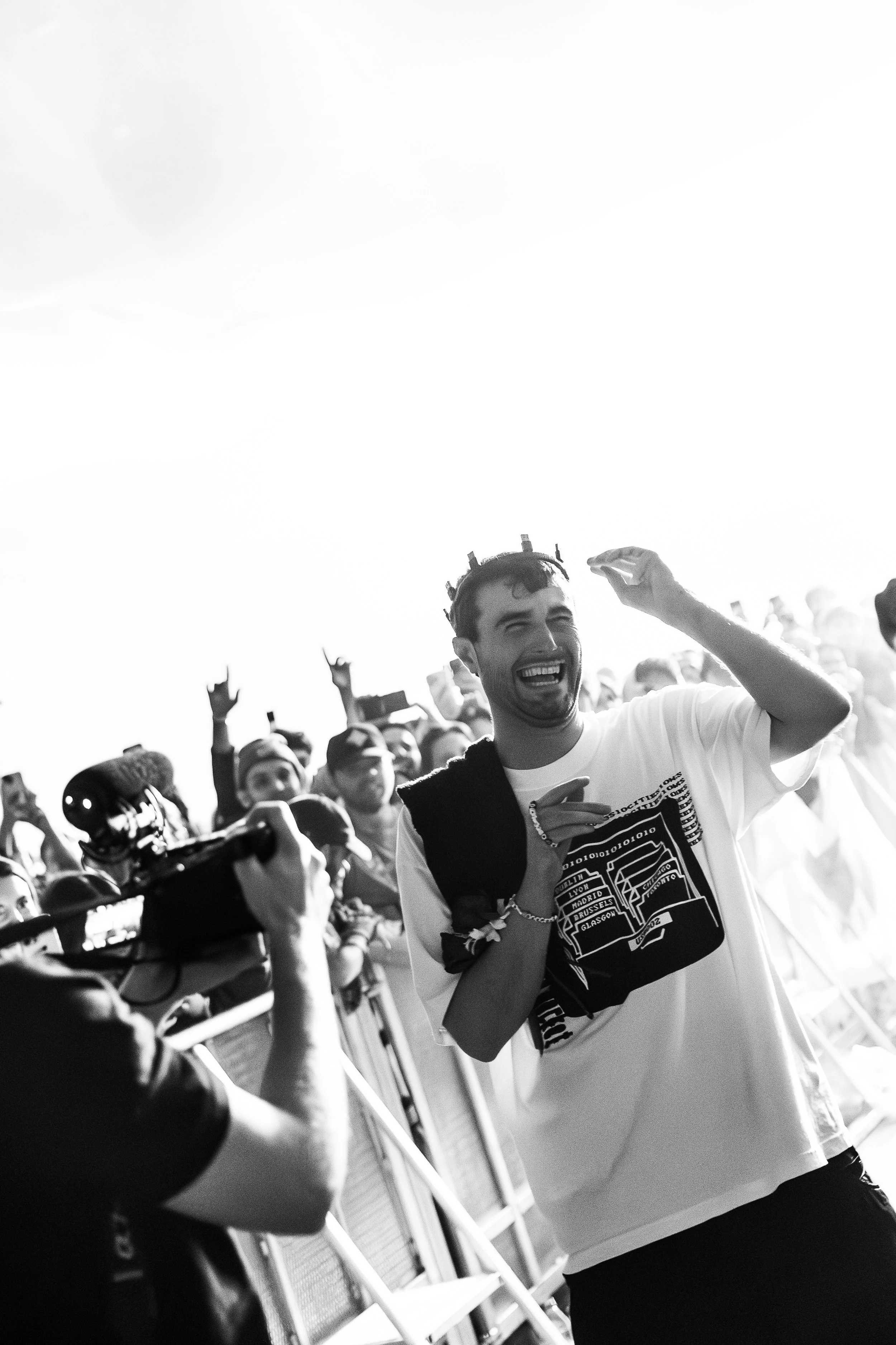 Fred Again at a concert or event, smiling and raising his hand, with a crowd in the background.