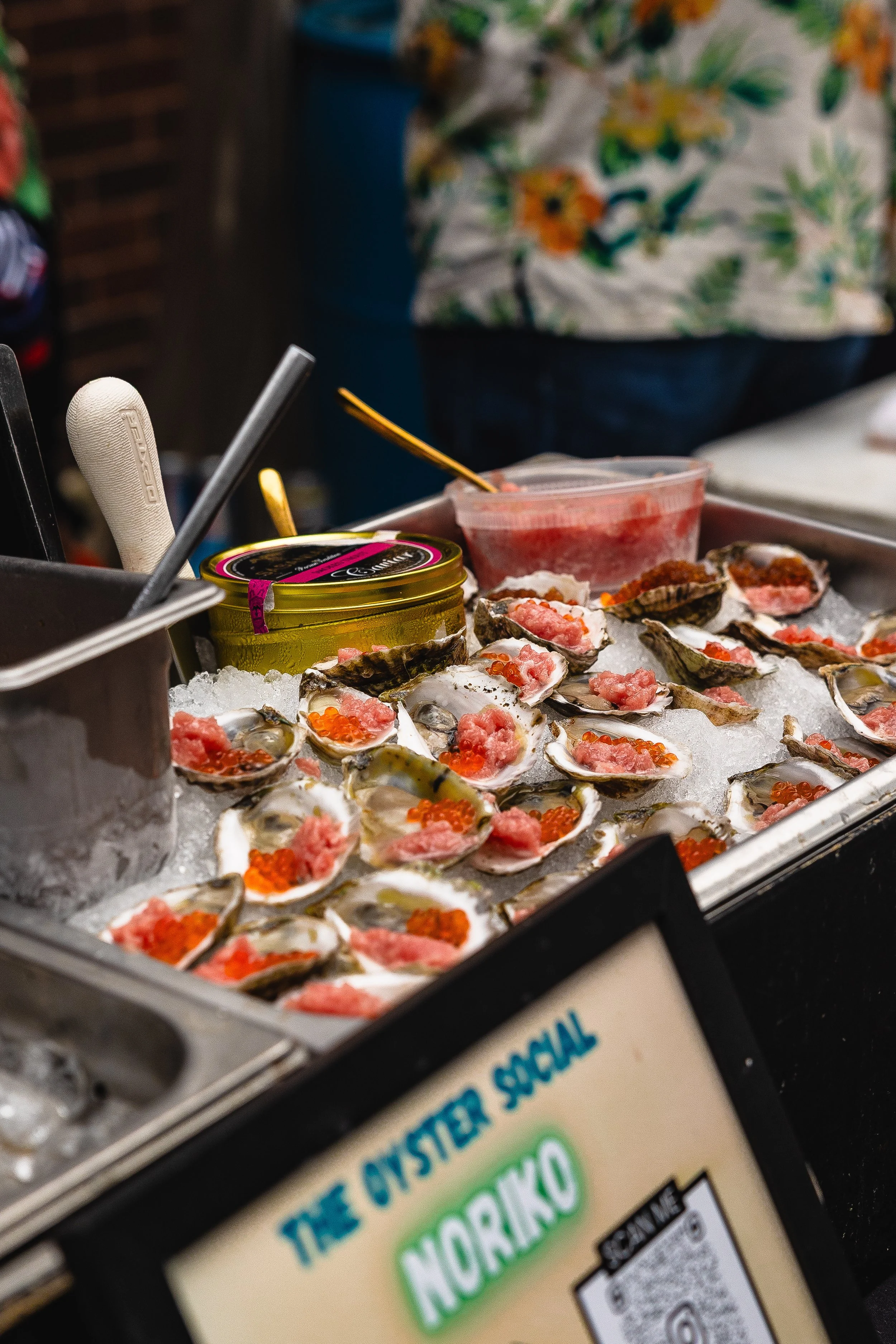 Fresh oysters on ice topped with pink mignonette sauce and orange fish roe, displayed at a seafood market stand.