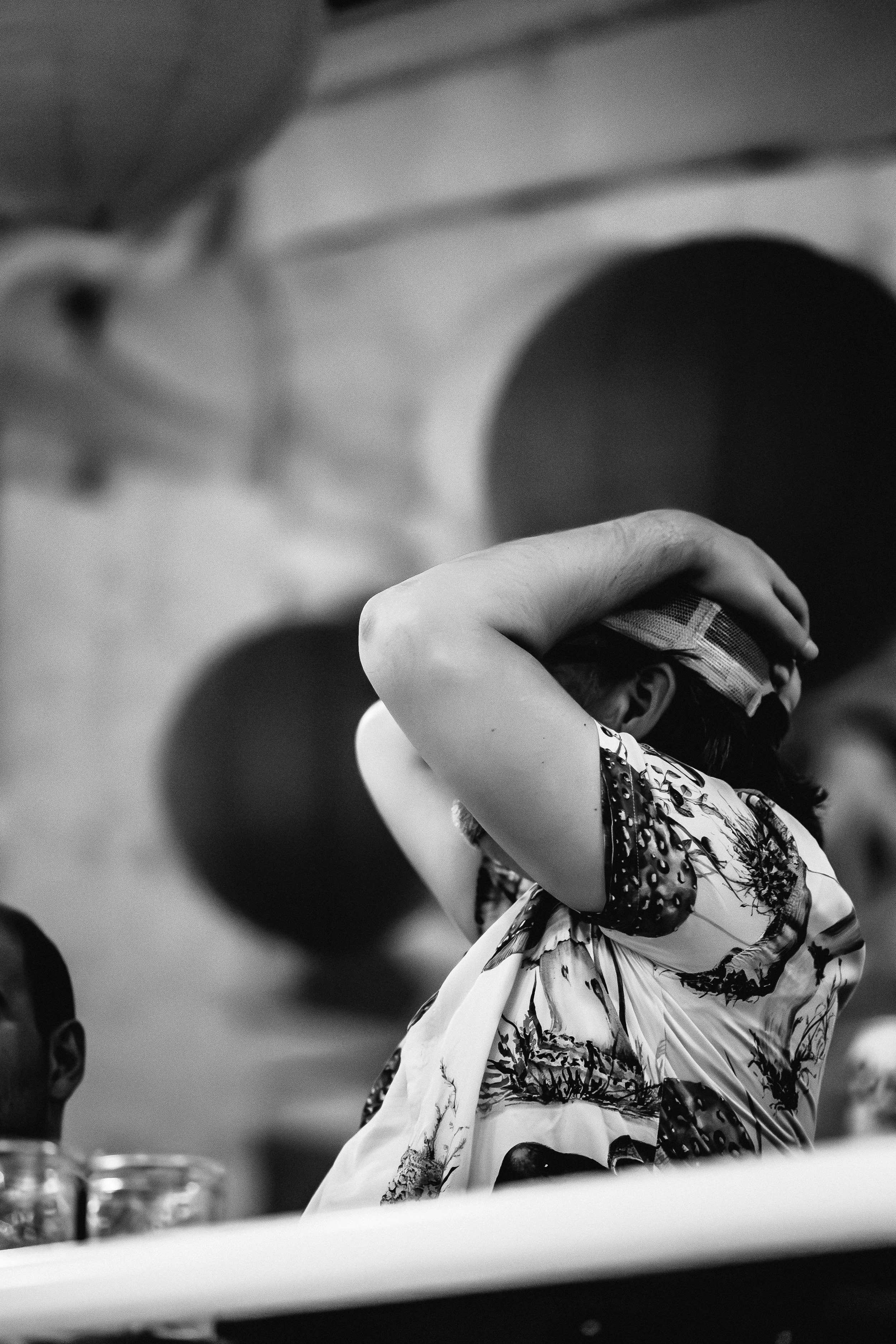 A person wearing a patterned shirt with their arms raised and hands on their head, with a hat, in a scene with large circular shapes in the background, black-and-white photo.