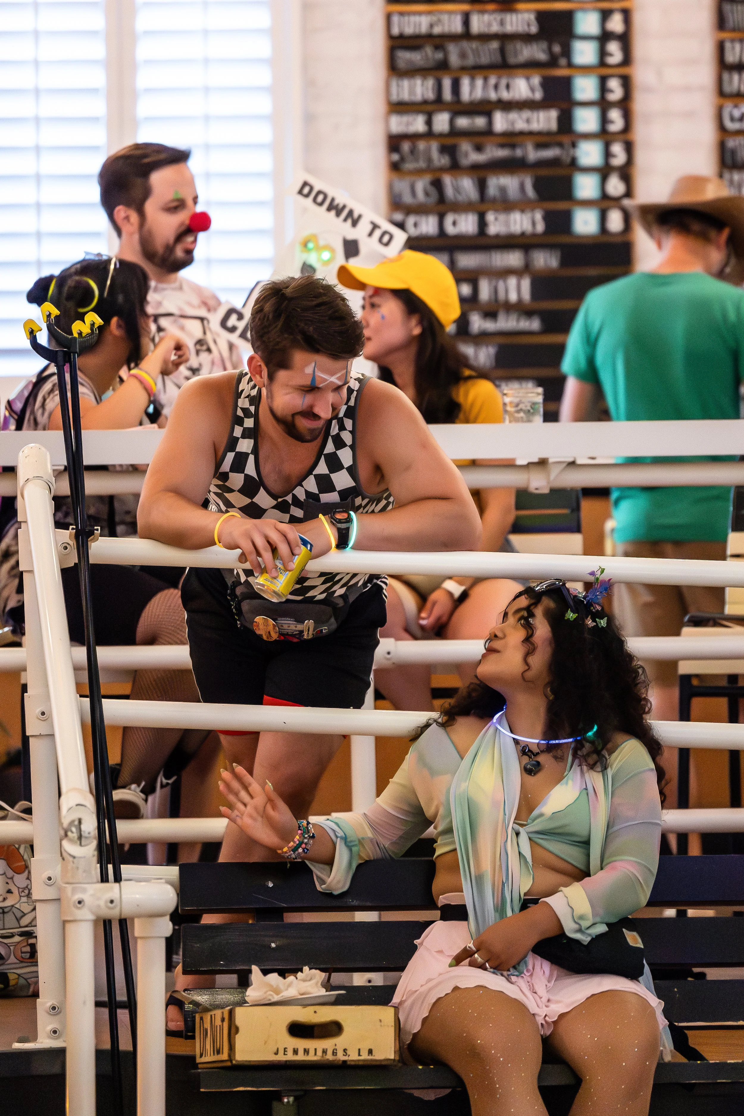 Group of young people dressed in colorful and playful outfits at a party, some engaging in conversation, with a festive and lively atmosphere.