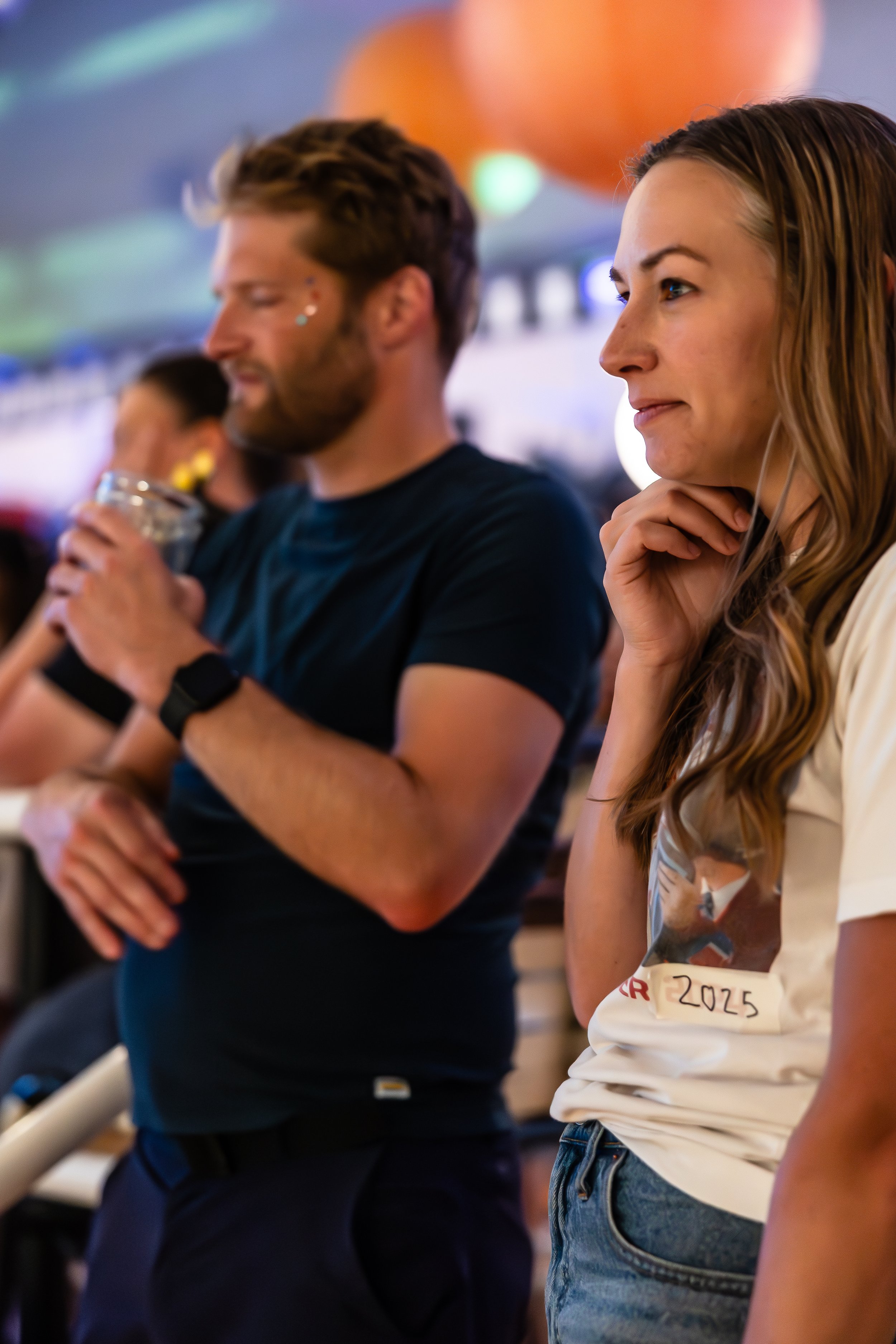 People attending an indoor event, some holding drinks, with a colorful lighting background.