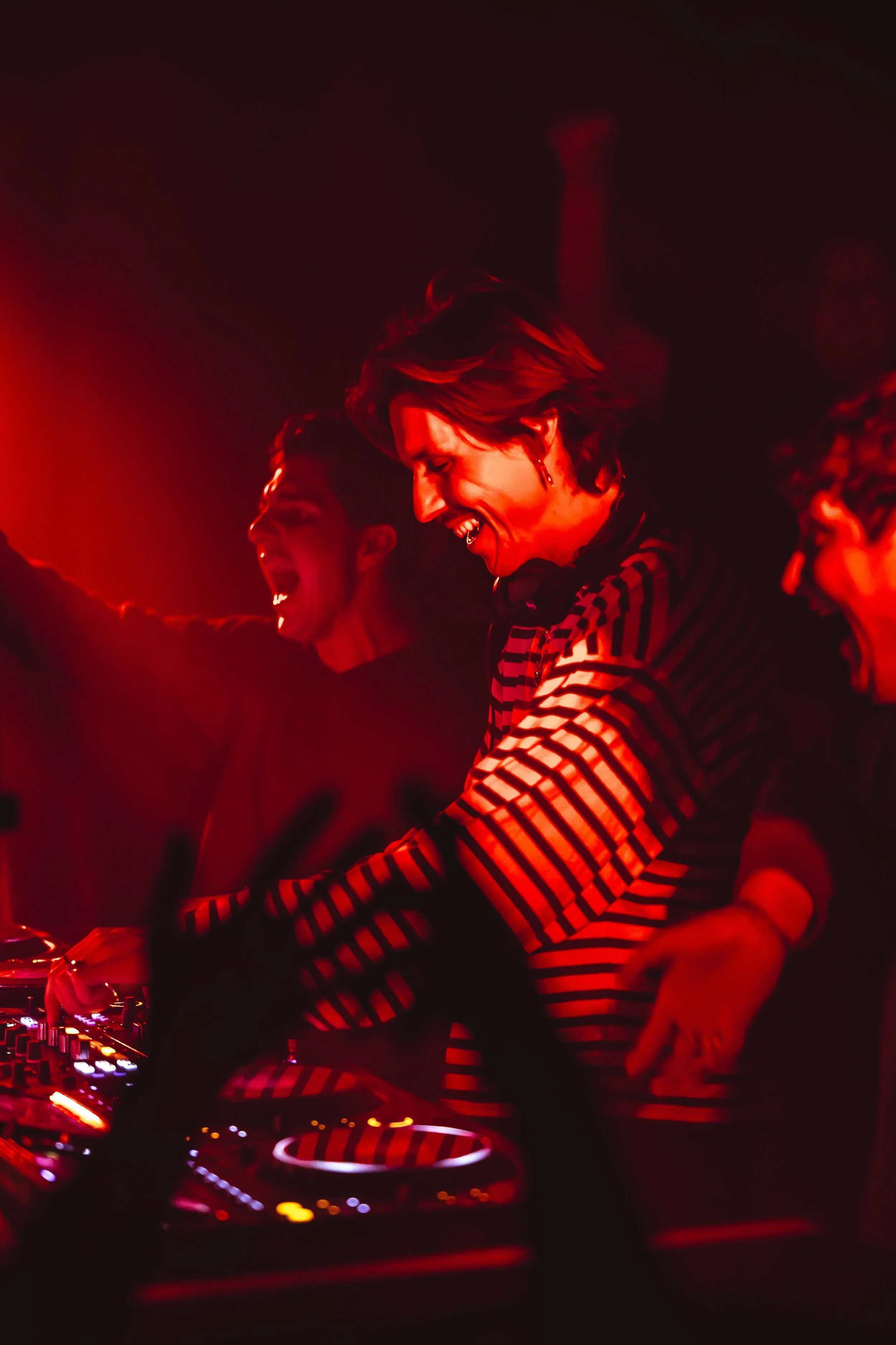 People enjoying a DJ music set in a club with red lighting.