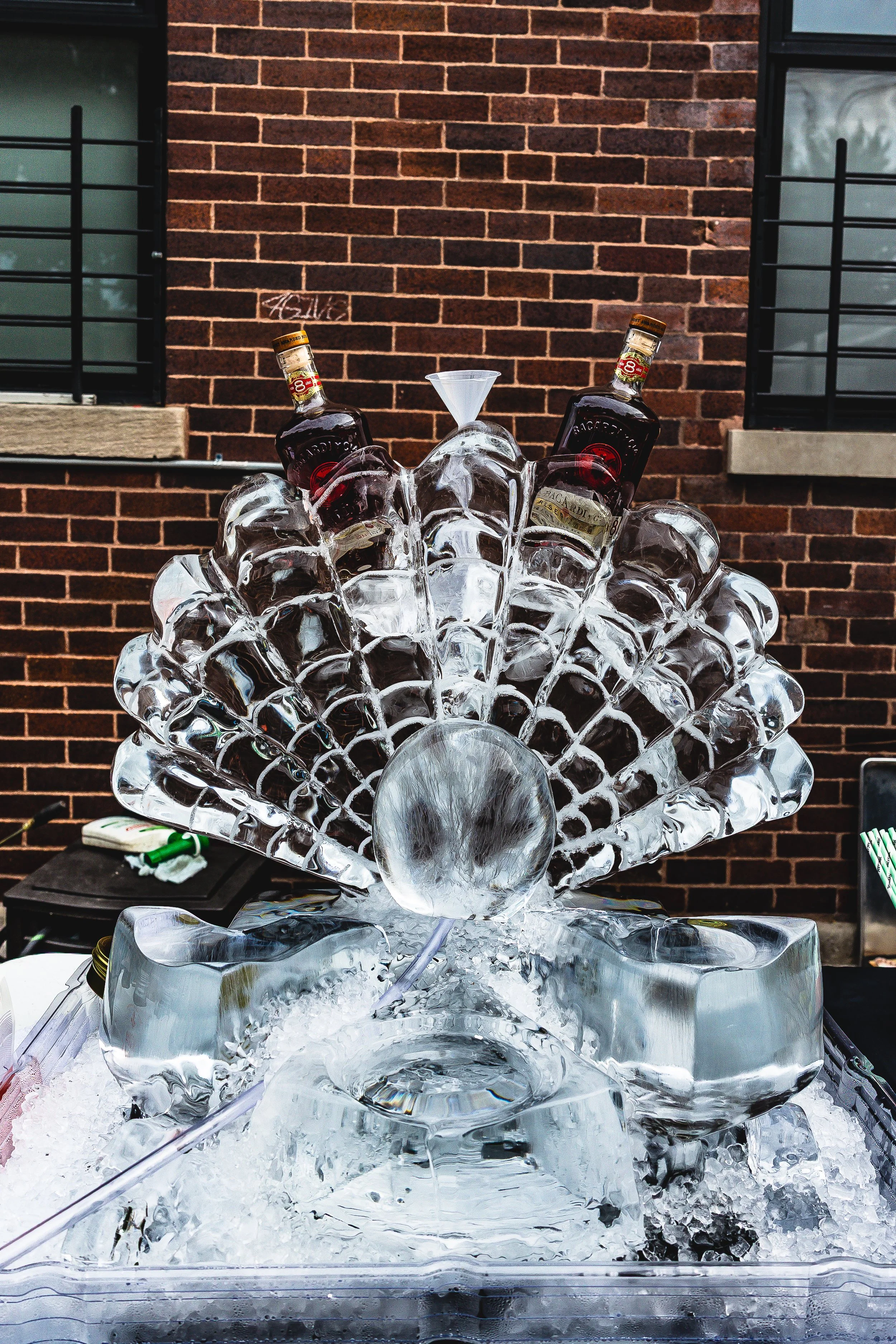 Ice sculpture featuring a fan shape with two liquor bottles at the top, set against a brick wall background.