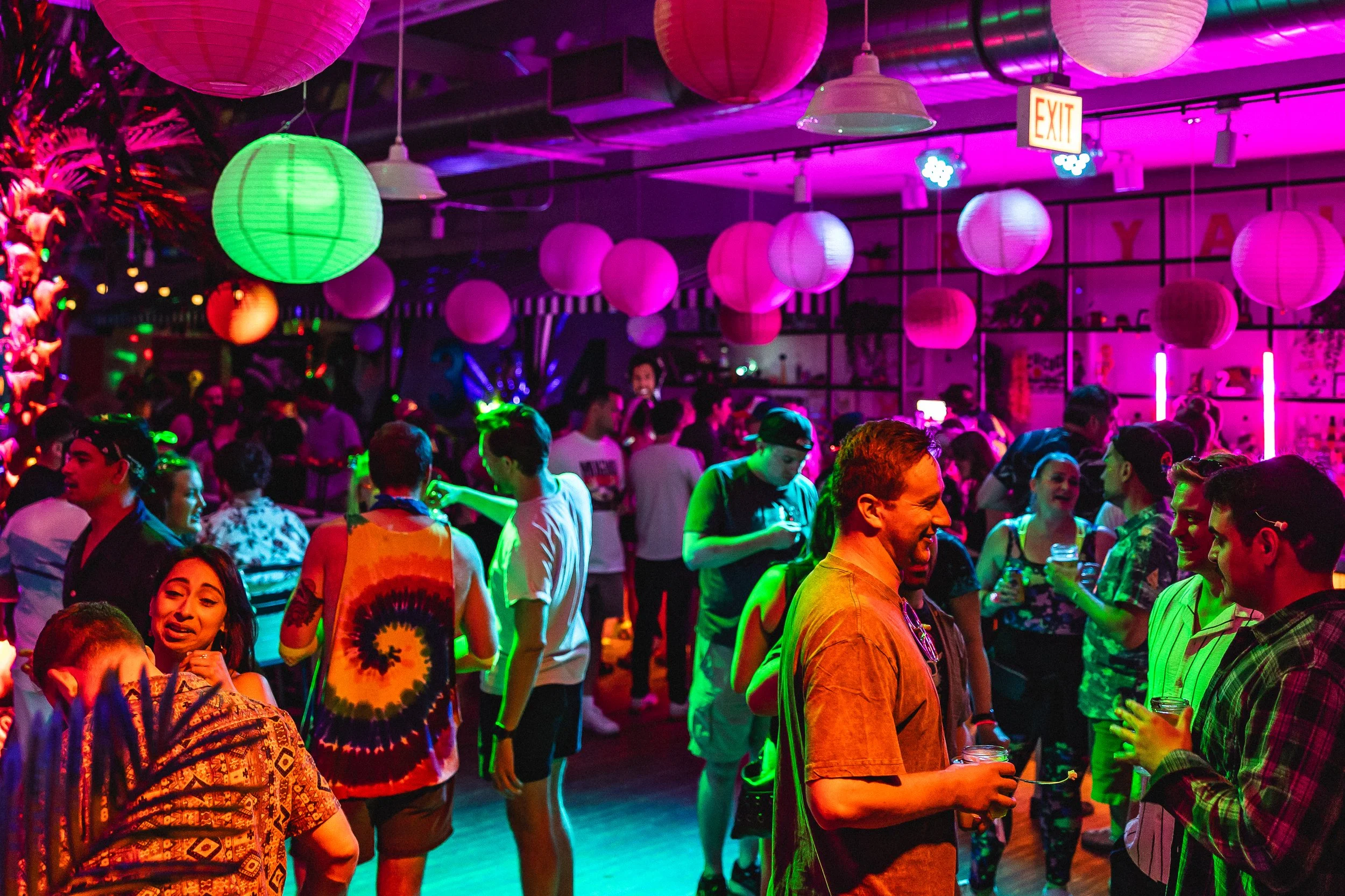 People dancing and socializing at a lively party with colorful paper lanterns and neon lights.