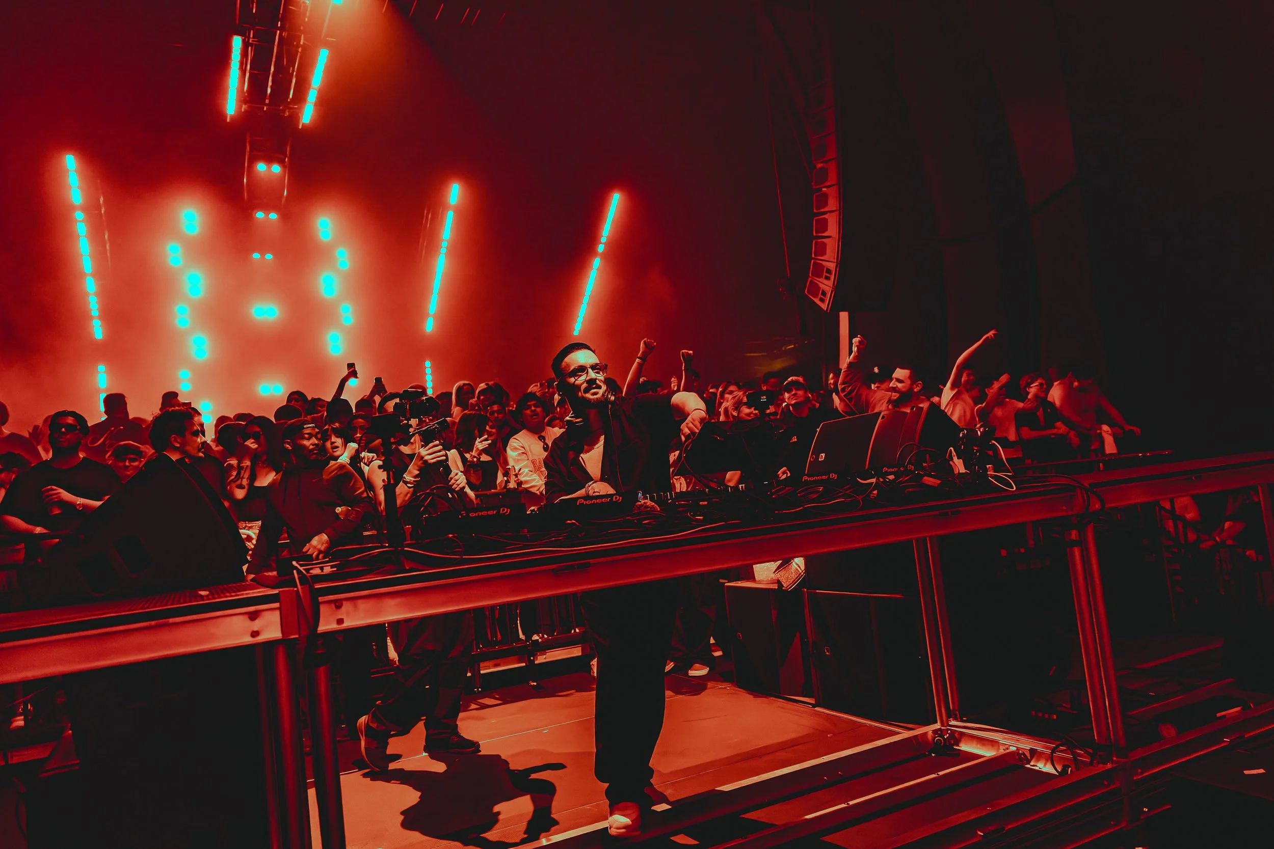 A DJ performing at a concert with a crowd enjoying the music, illuminated by vibrant red and blue lights.