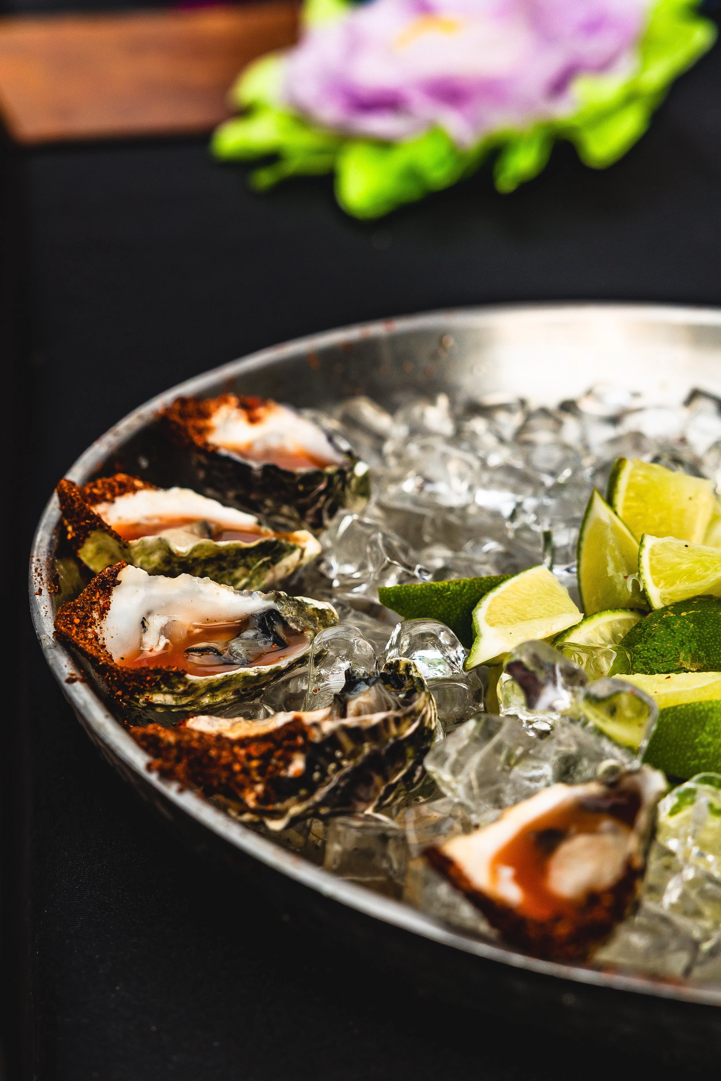 Close-up of fresh oysters with lime wedges on ice in a metal tray.