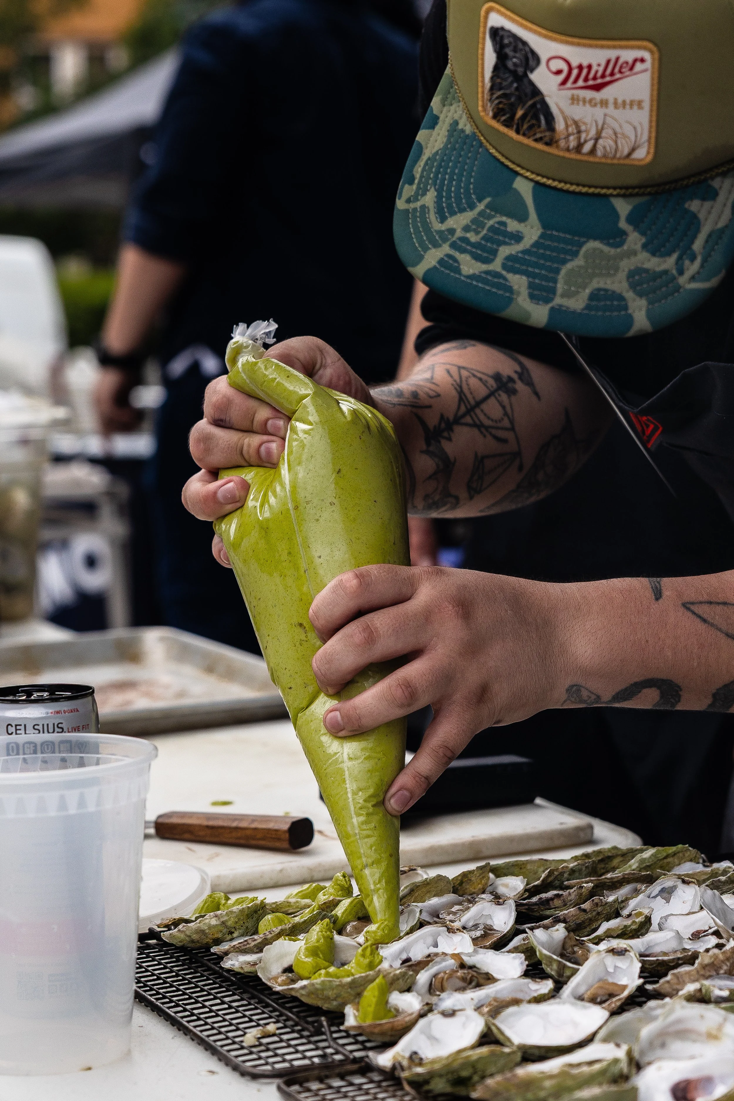 Person shucking oysters with a green piping bag on a table covered with oysters.