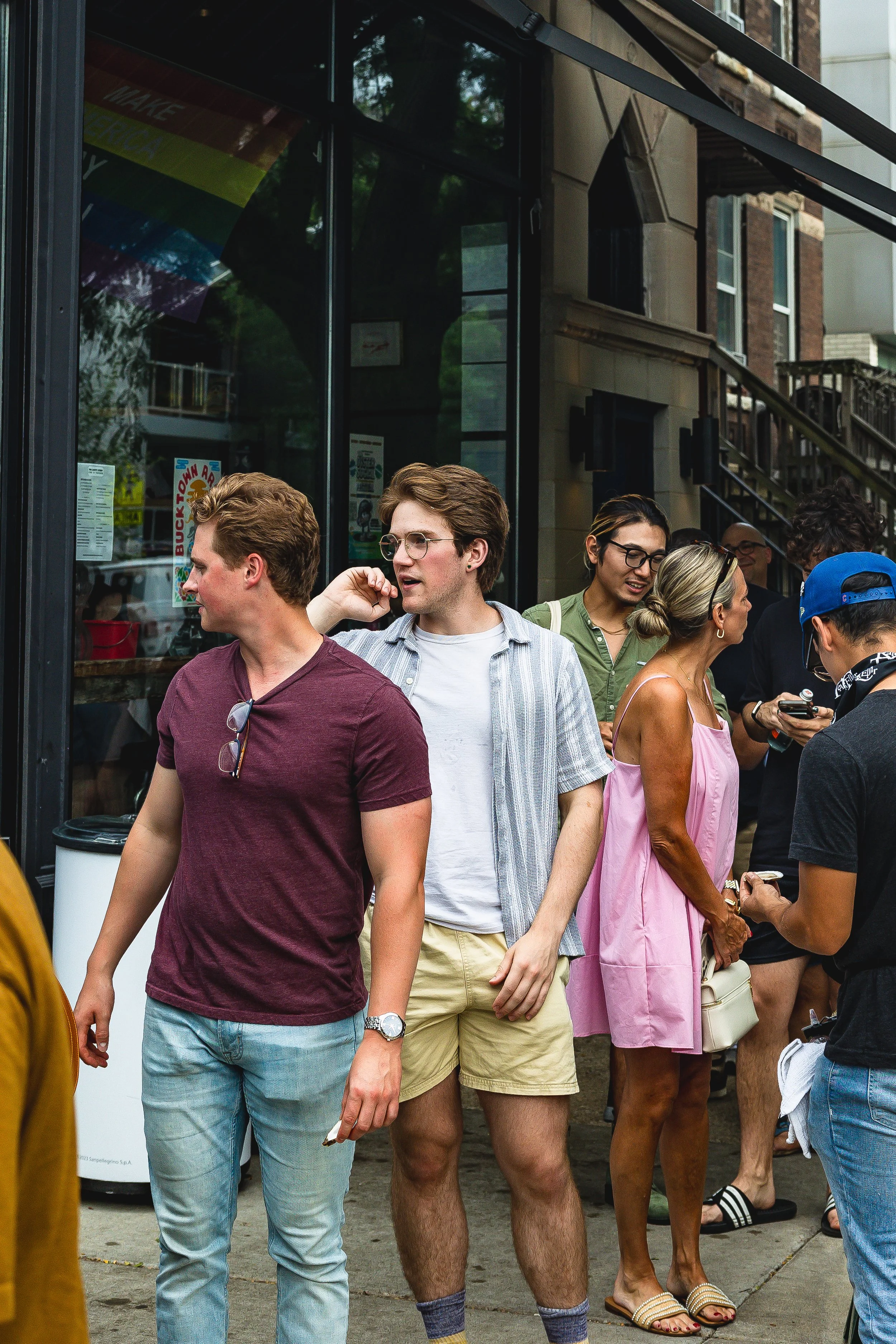 A group of people standing outside a building, socializing, dressed in casual summer clothing.