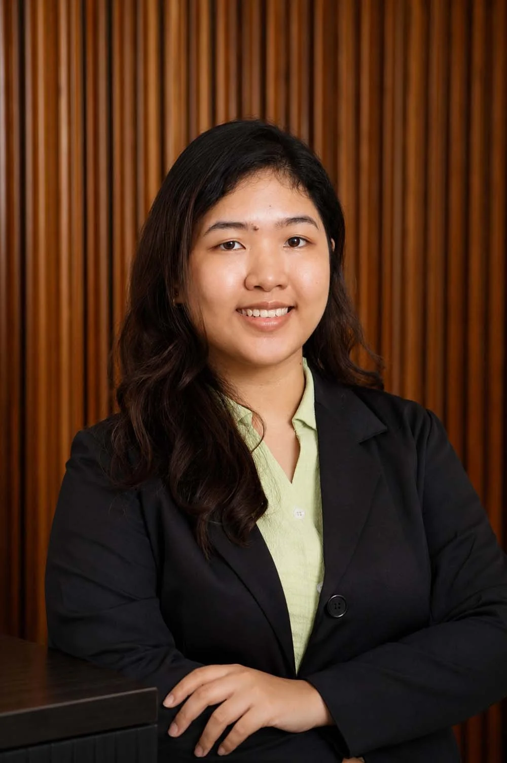 Portrait of a smiling person wearing a black blazer over a light green shirt against a plain background.