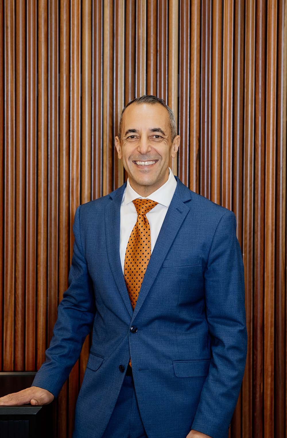 financial adviser in Sydney wearing a suit and red tie, smiling while standing in a professional office setting with greenery, representing strategic thinking and personalised financial advice.