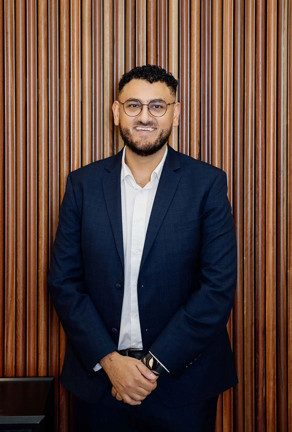 Finanical Advisor Kyrillos Ghaly in a dark suit and white shirt smiling against a light background.