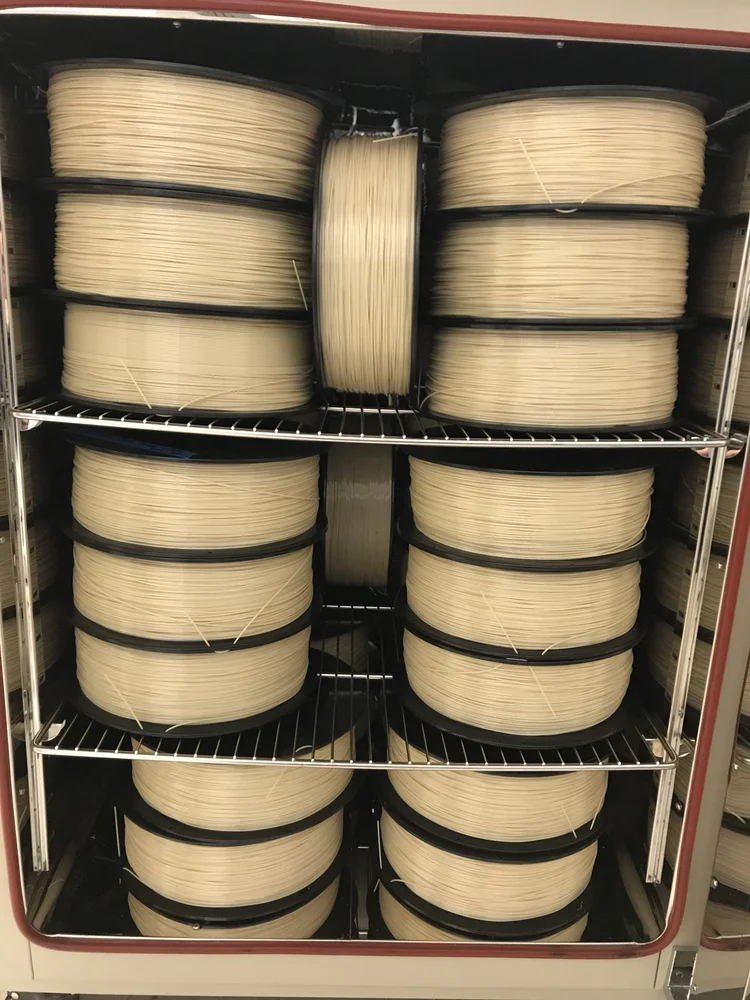 Multiple large black spools of natural high-temperature filament drying and staged in inventory at NEXT 3DP