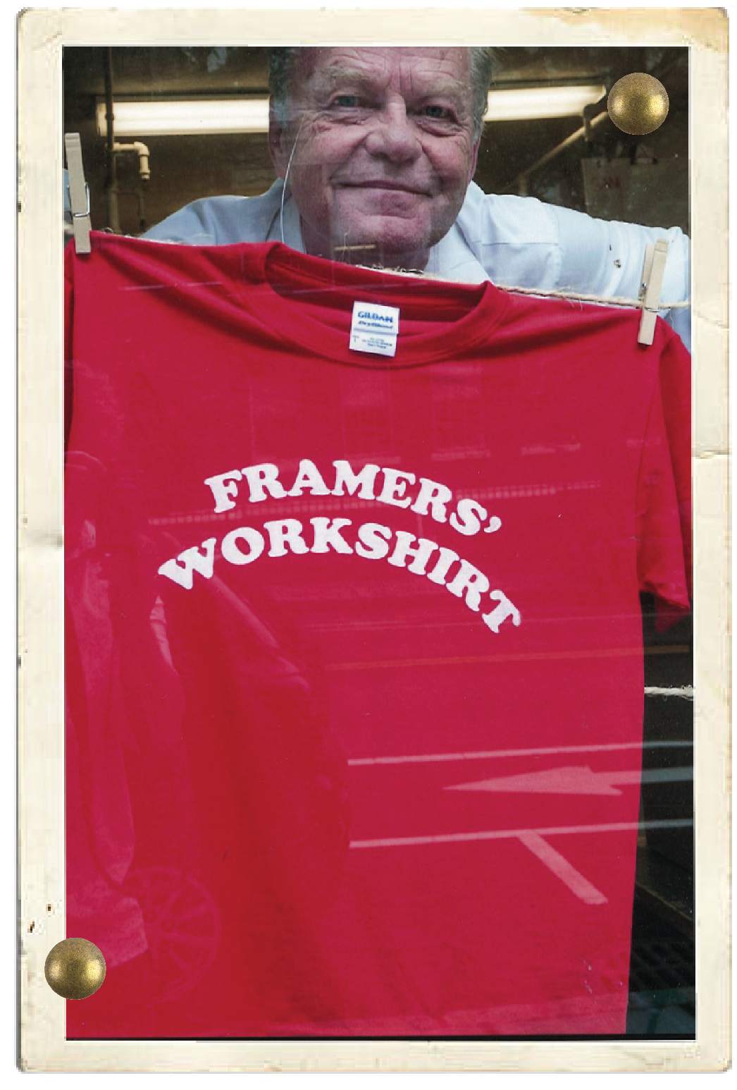 The original frame shop owner, a man smiling behind a red T-shirt that reads 'FRAMERS, WORKSHIRT' hanging on a laundry line with clothespins.