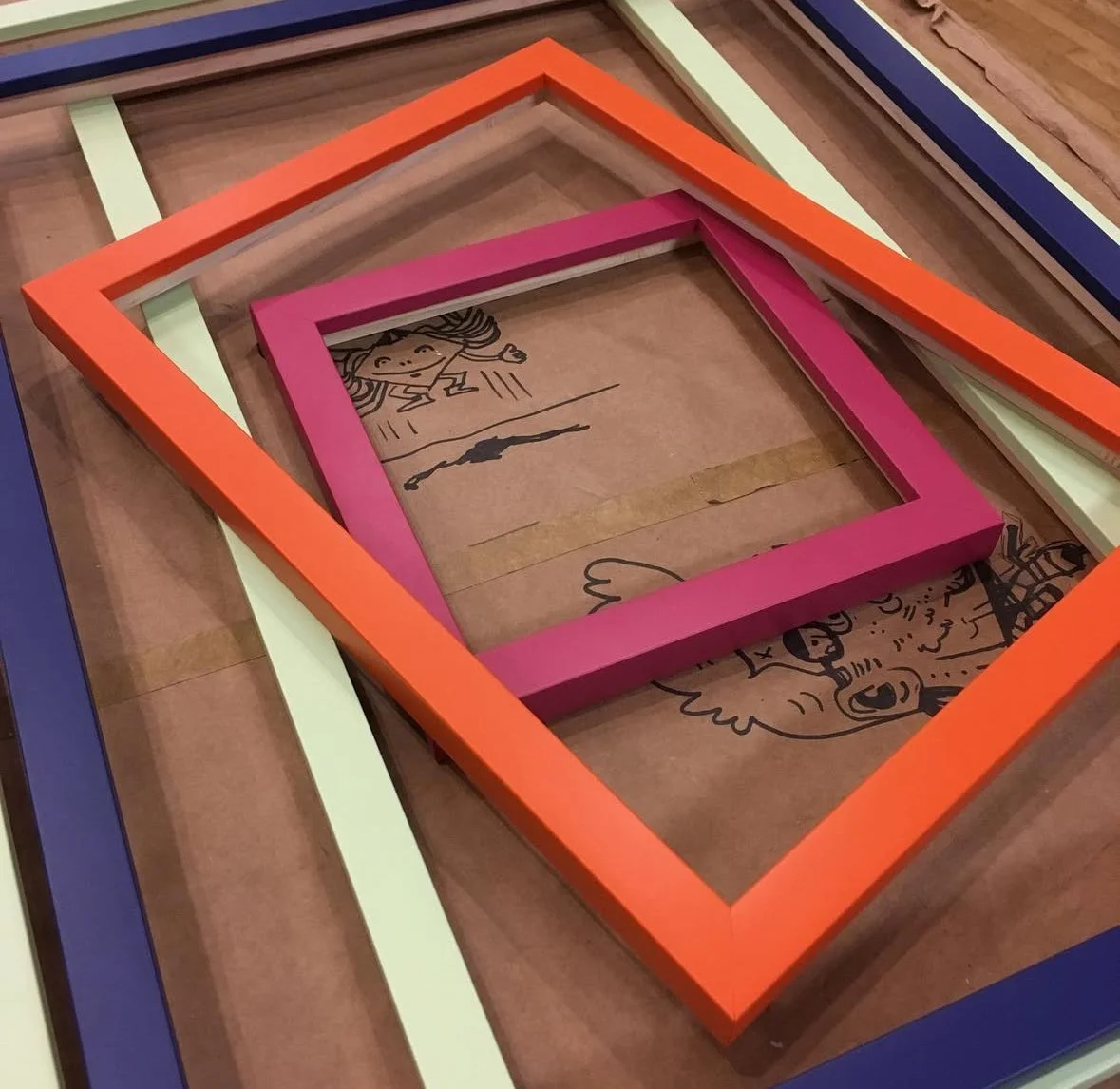 Colorful picture frames arranged in overlapping manner, with a child's drawing underneath on a brown paper surface.