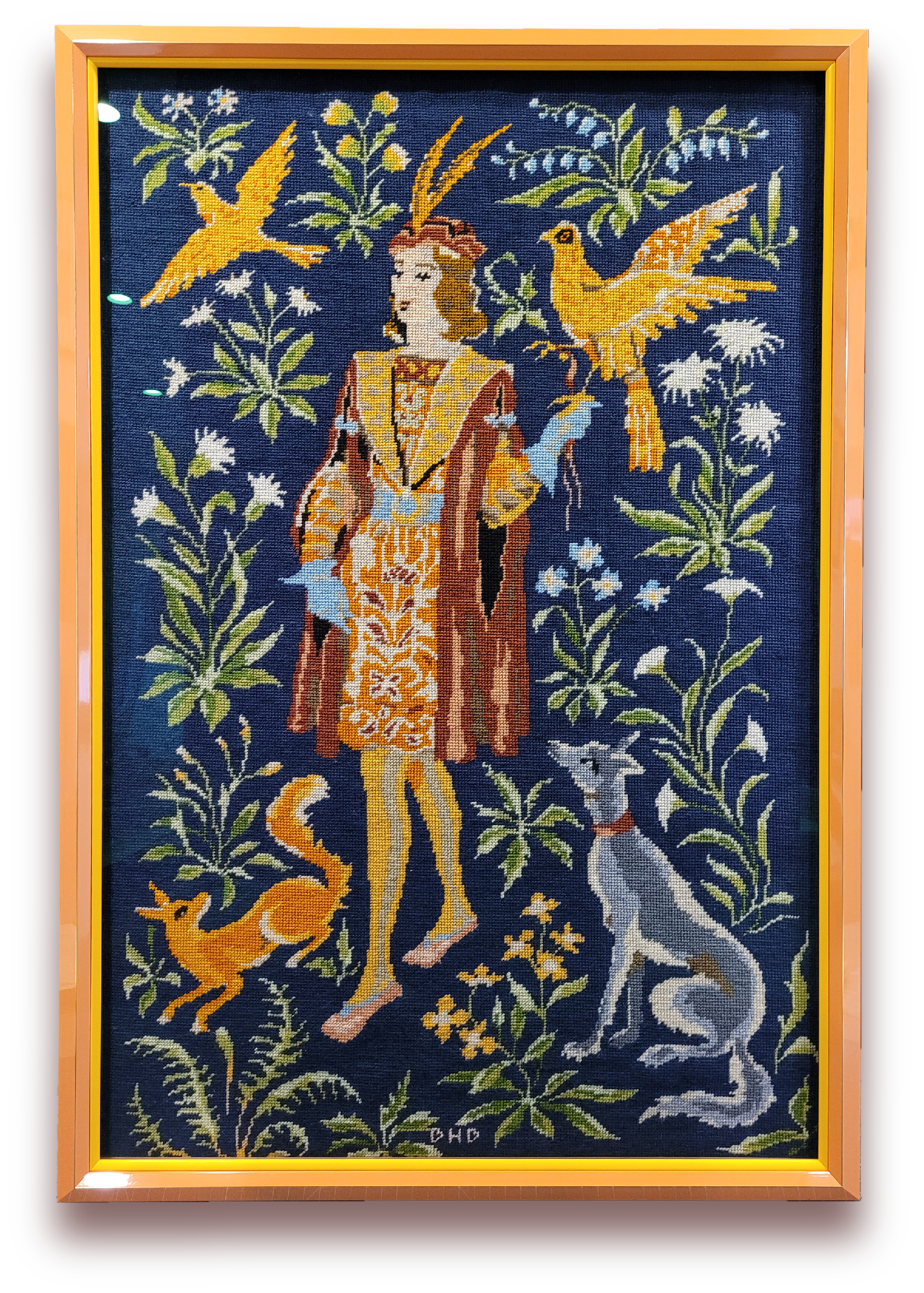Cross-stitch tapestry depicting a woman in historical clothing surrounded by birds, a dog, and floral elements on a dark blue background.