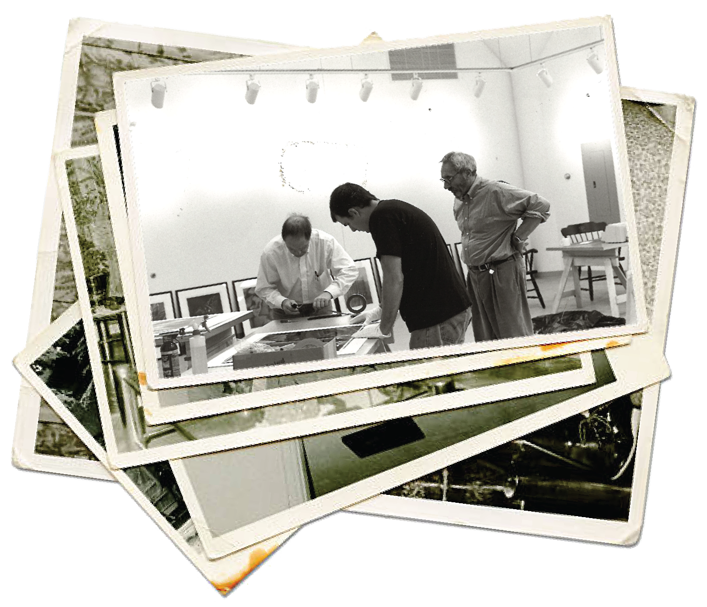 Old old black and white photograph of three men at the original frame shop location, examining artwork or photographs on a table. The room has framed pictures on the wall and studio lighting.