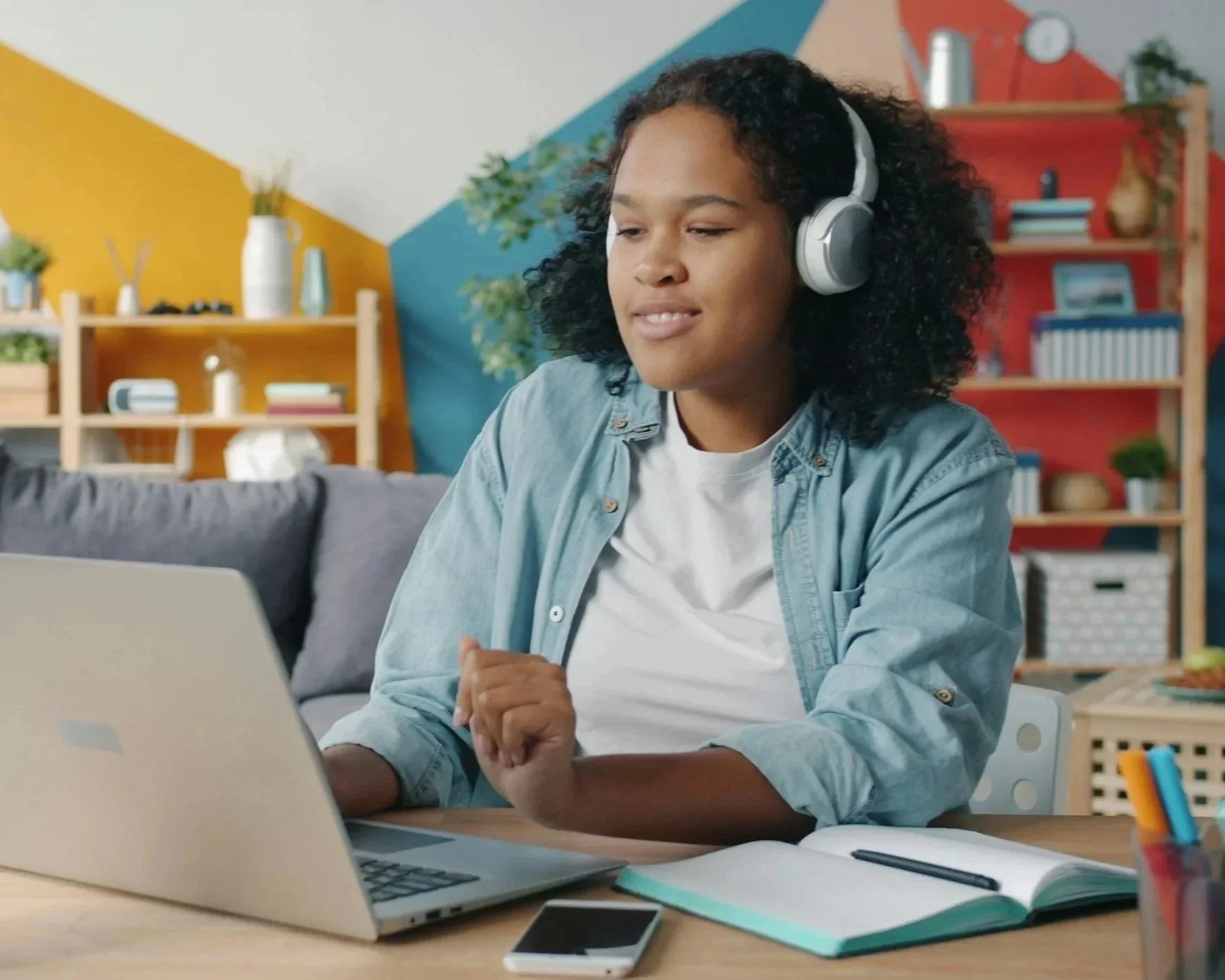 Teenage girl sitting at a computer with headphones on.