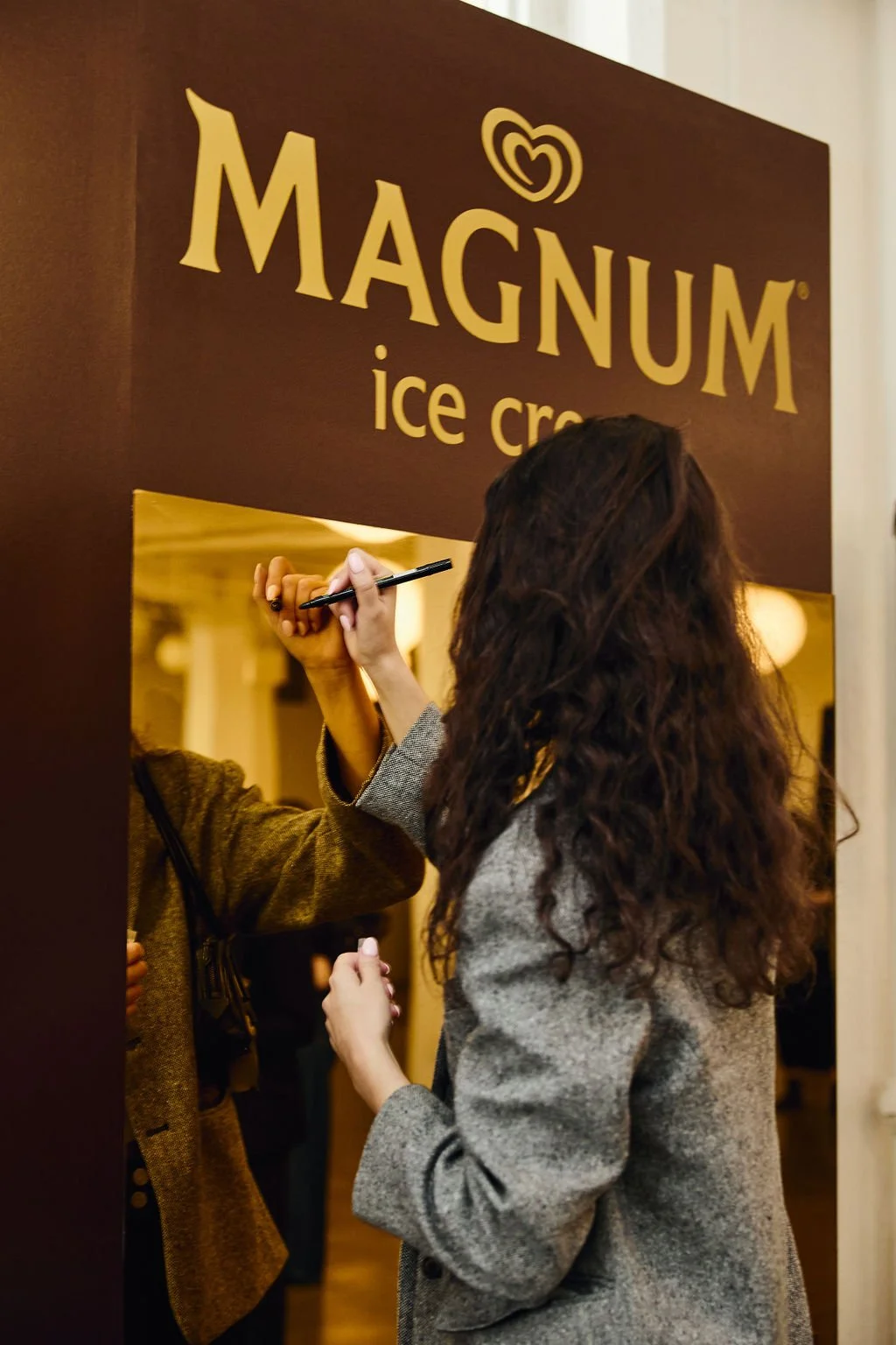 A woman with long, curly hair signing an ice cream stand with a sign that reads 'Magnum ice cream'.