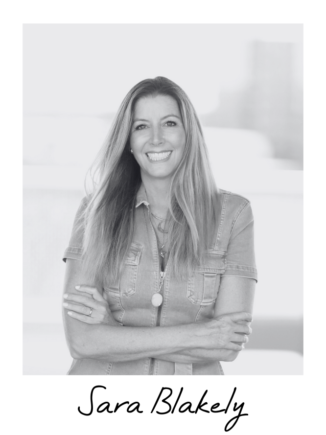 Black and white photo of a woman smiling with crossed arms, wearing a denim shirt and jewelry, with the name Sara Blakely written below.