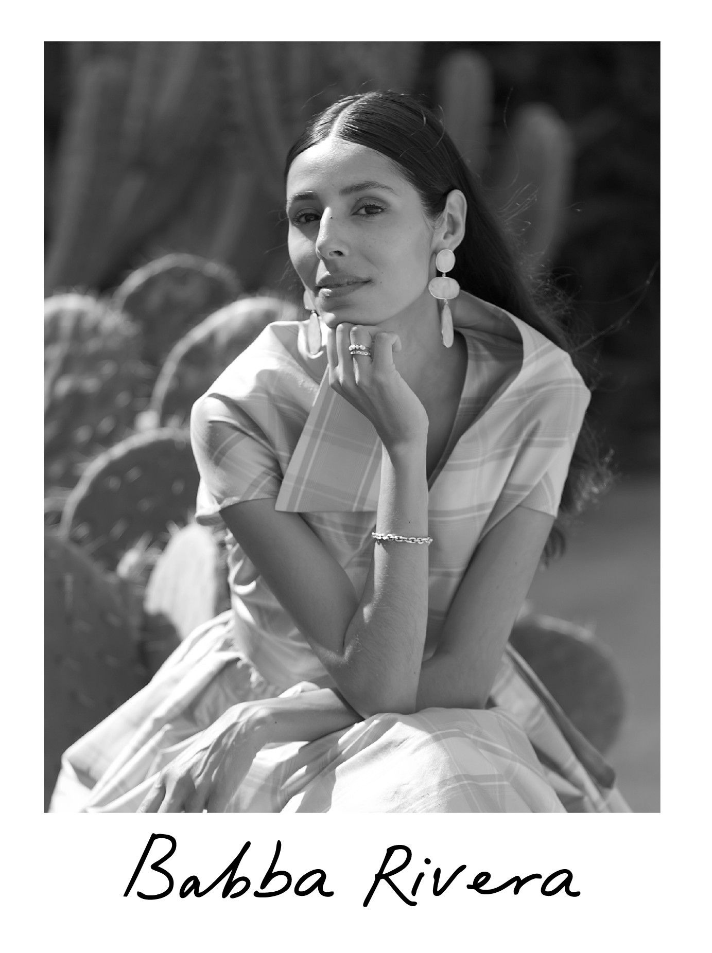 Black and white portrait of a woman with long dark hair, wearing earrings, a bracelet, and a plaid dress, sitting outdoors with a cactus in the background, and her hand resting on her chin. The text "Babba Rivera" is written at the bottom.