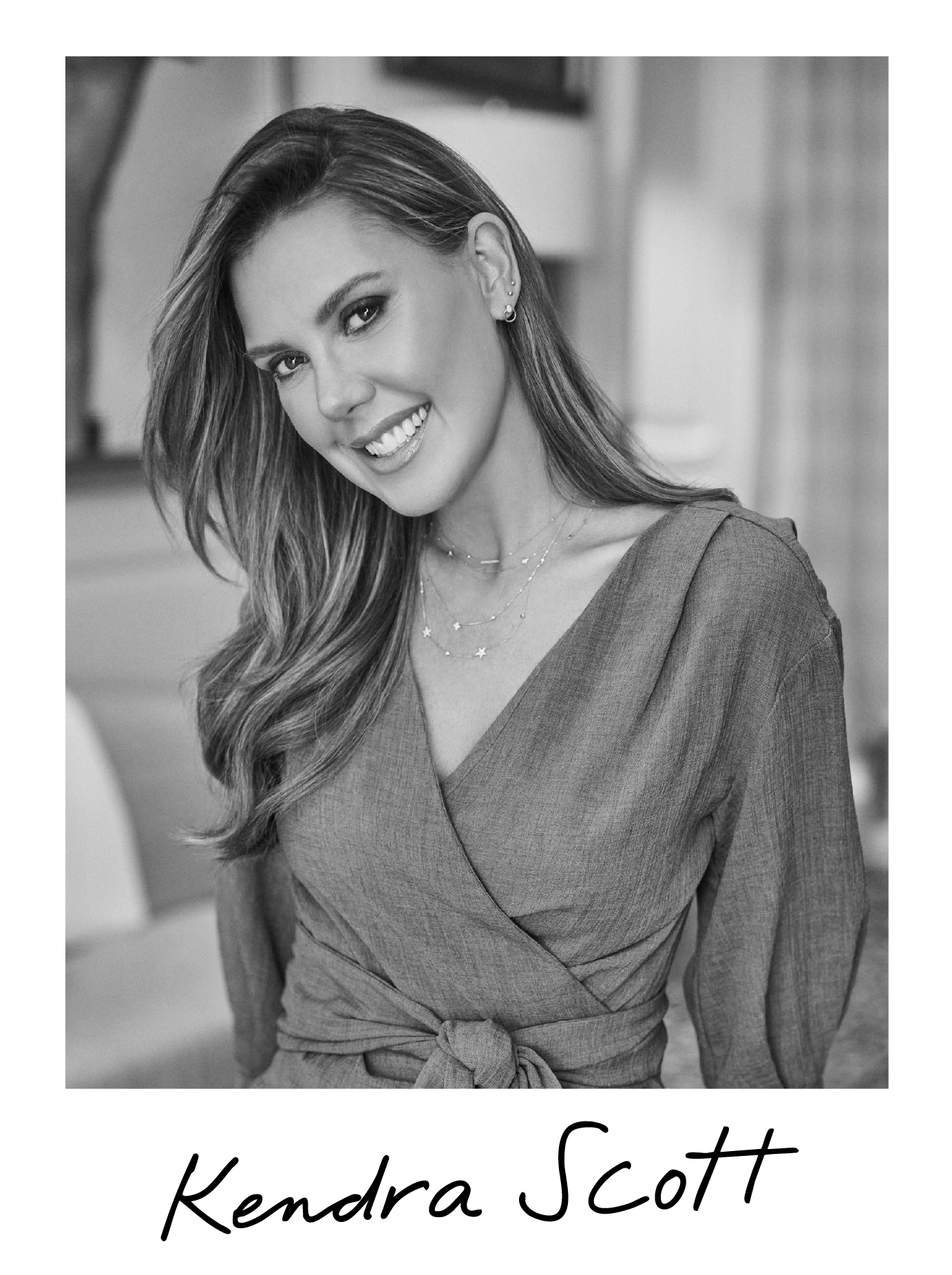 Black and white portrait of a woman smiling, with long wavy hair, wearing a wrap dress, layered necklaces, and earrings. Her name, Kendra Scott, is written in cursive at the bottom.