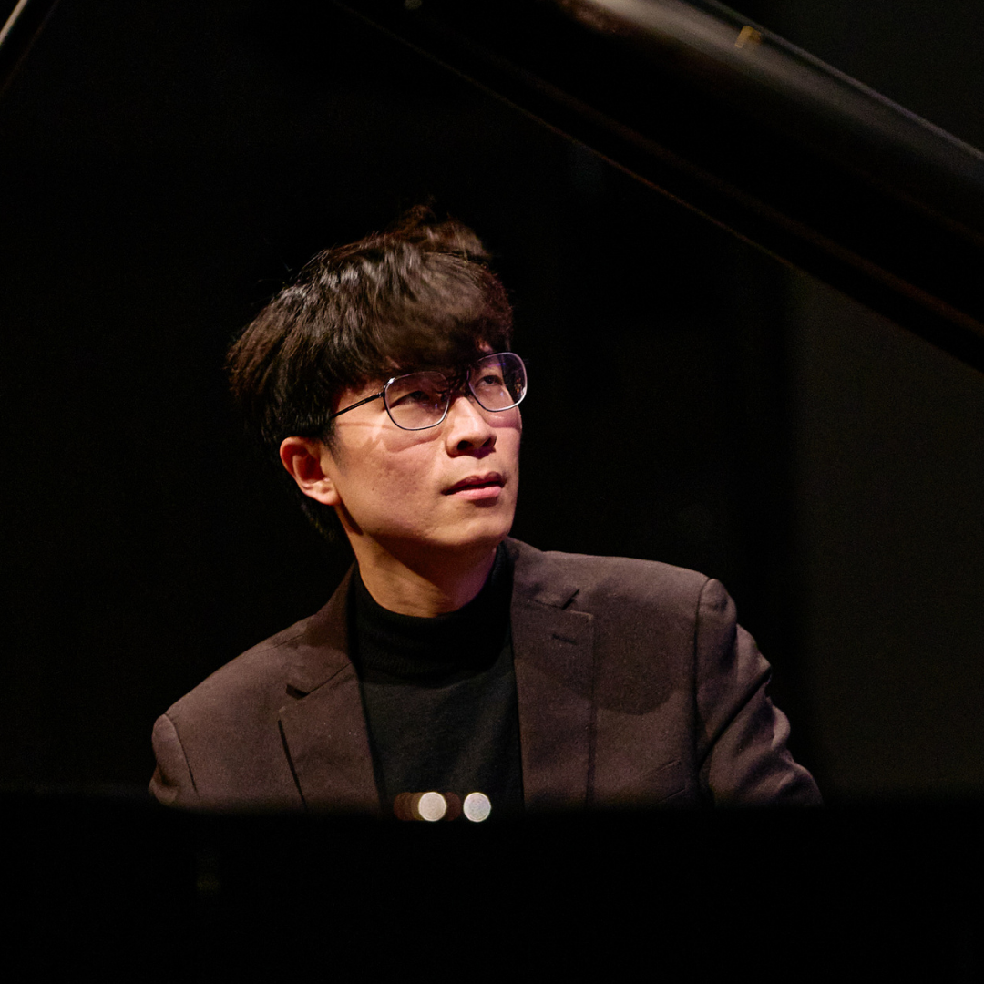 A person in a black suit playing a grand piano on stage.