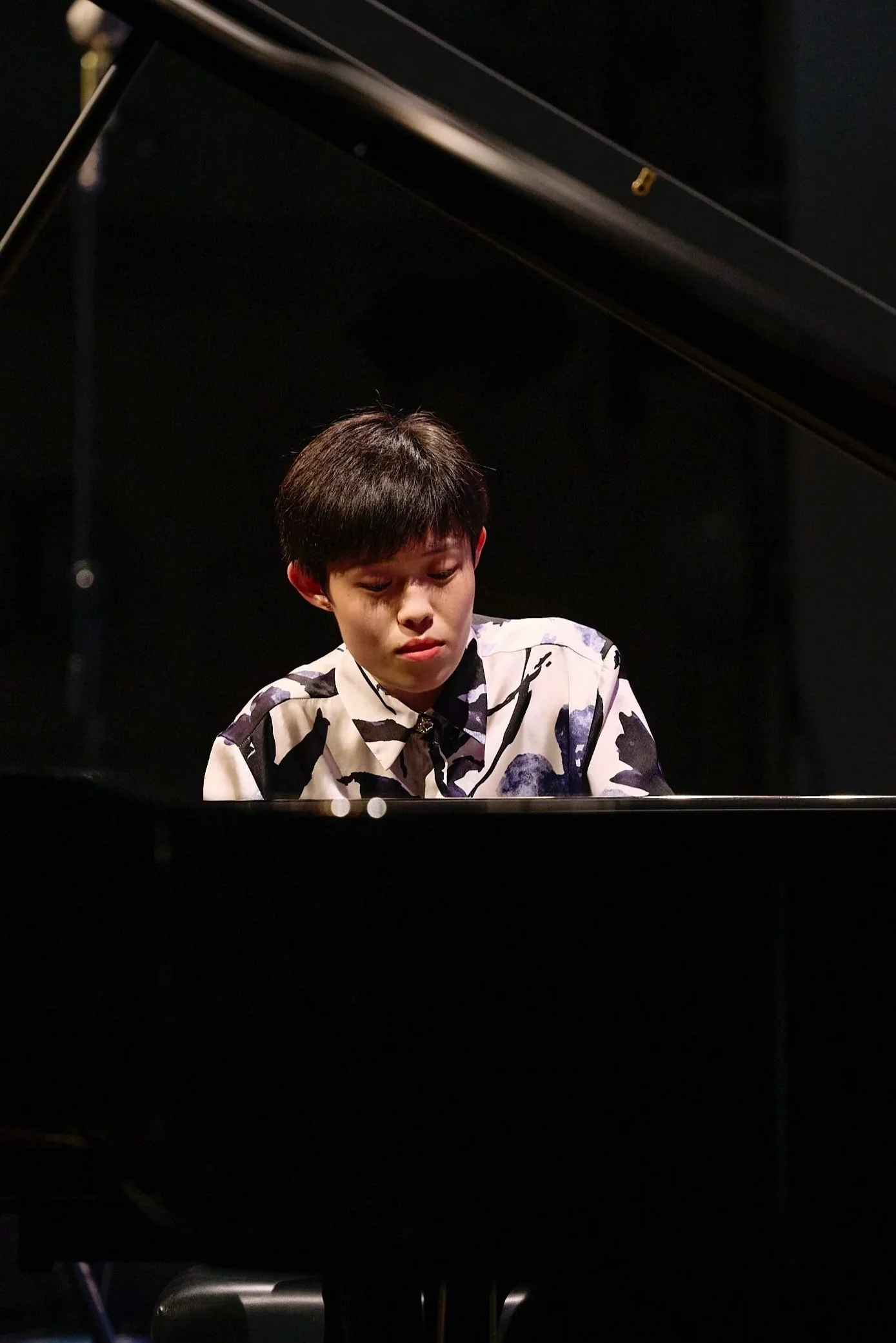 Person playing a grand piano, focusing on a performance on stage.