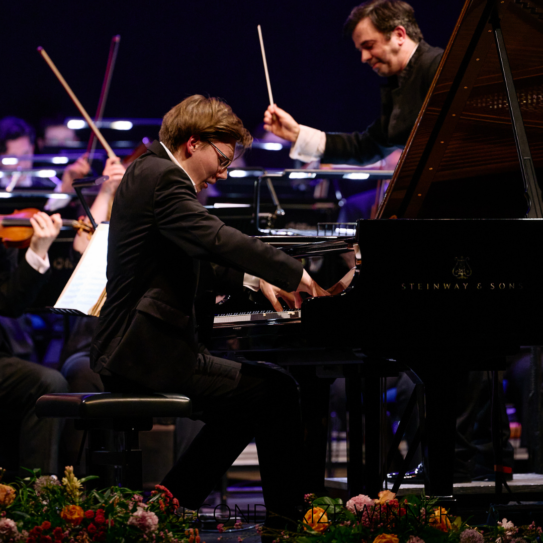 A man playing a grand piano passionately on stage, part of an orchestra performance