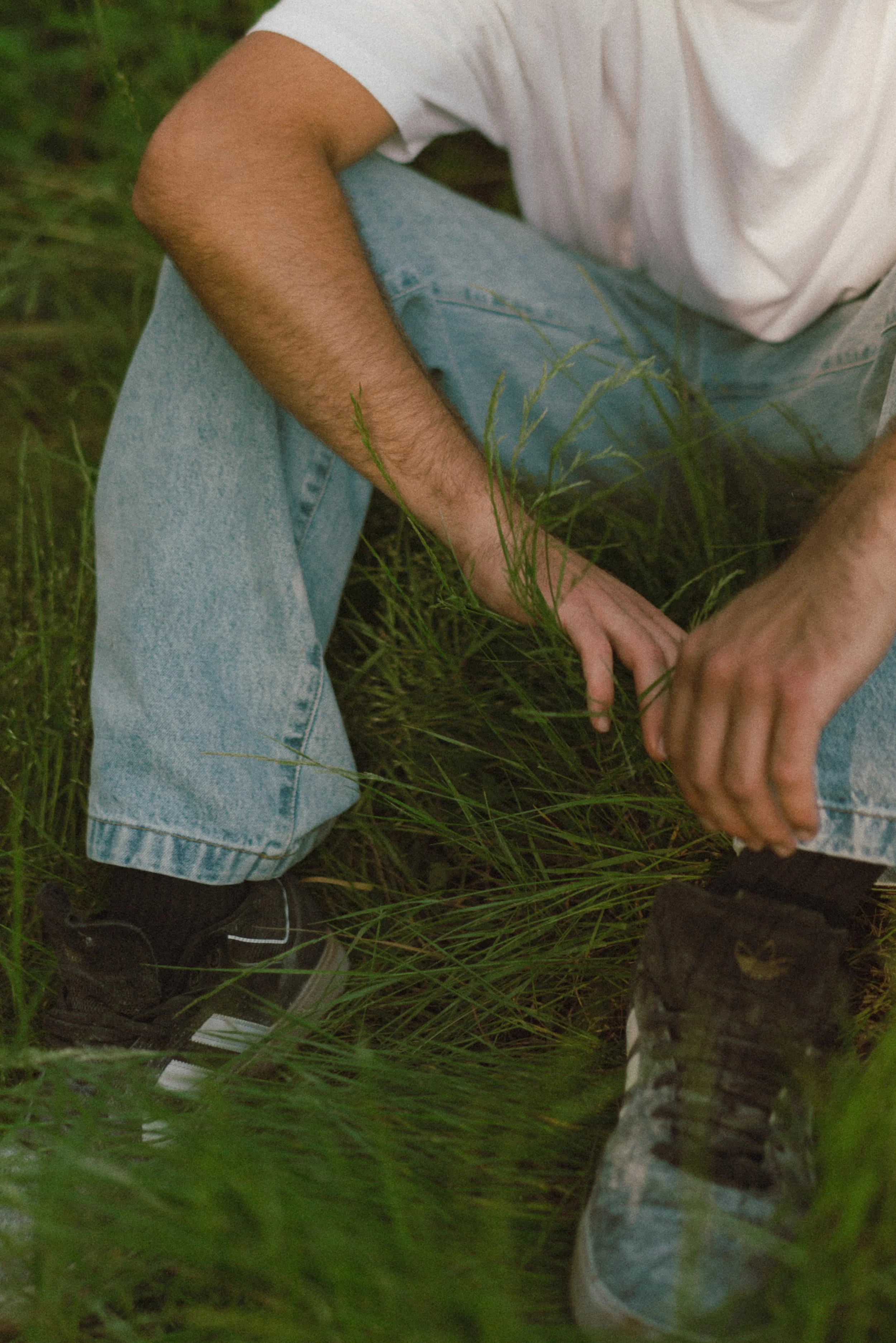 Personne assise dans l'herbe avec un jean bleu clair et des baskets noires.