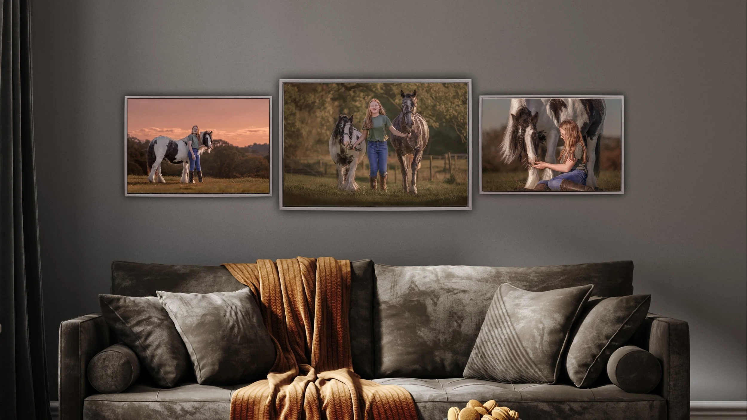 Three framed photos on a gray wall above a gray velvet sofa showing a girl with horses at sunset and daytime, with pillows and a brown throw blanket on the sofa.
