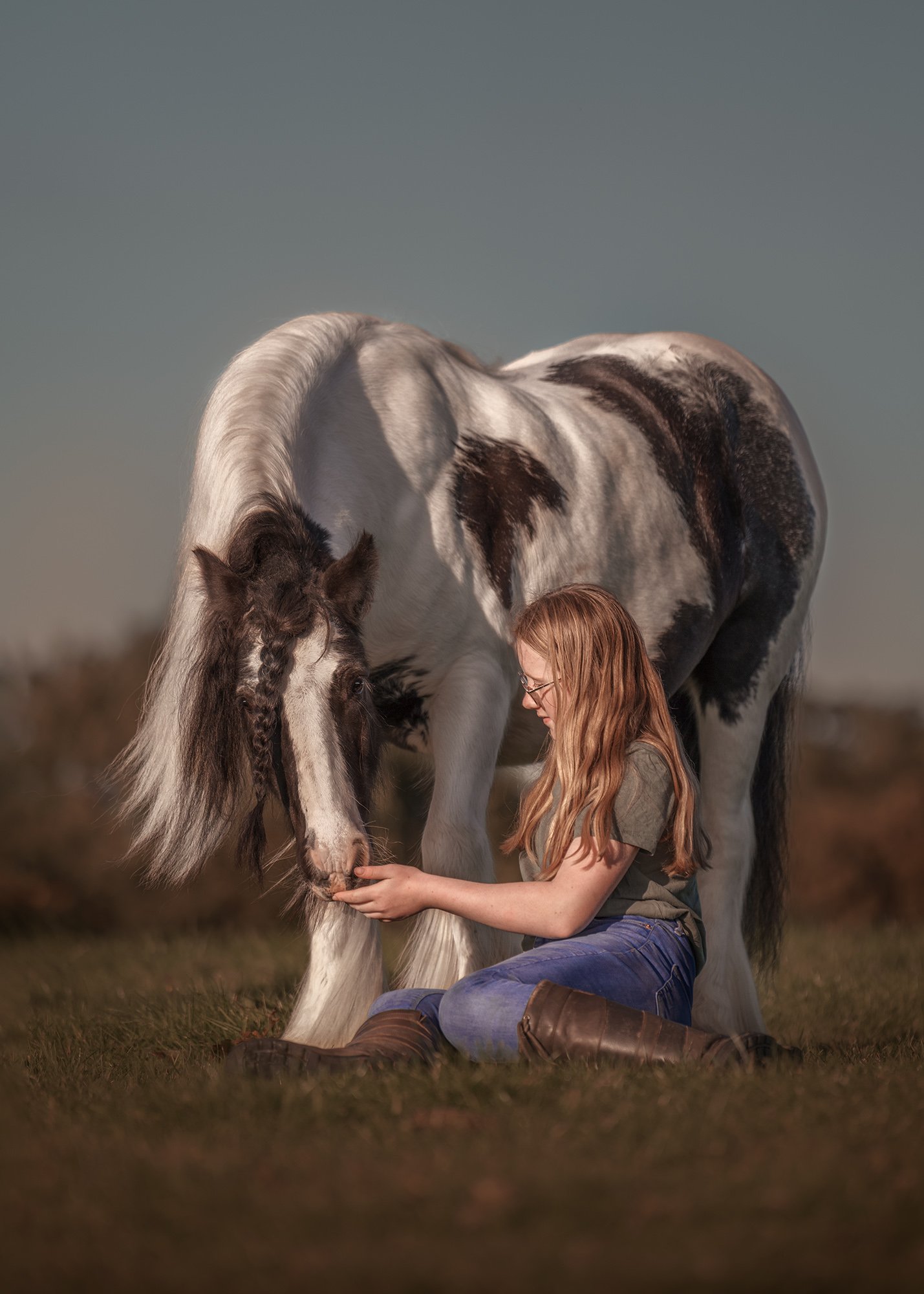 A young girl sits in the grass looking lovingly at her cob pony. Photographed by Frankie Adamson in Cumbria.