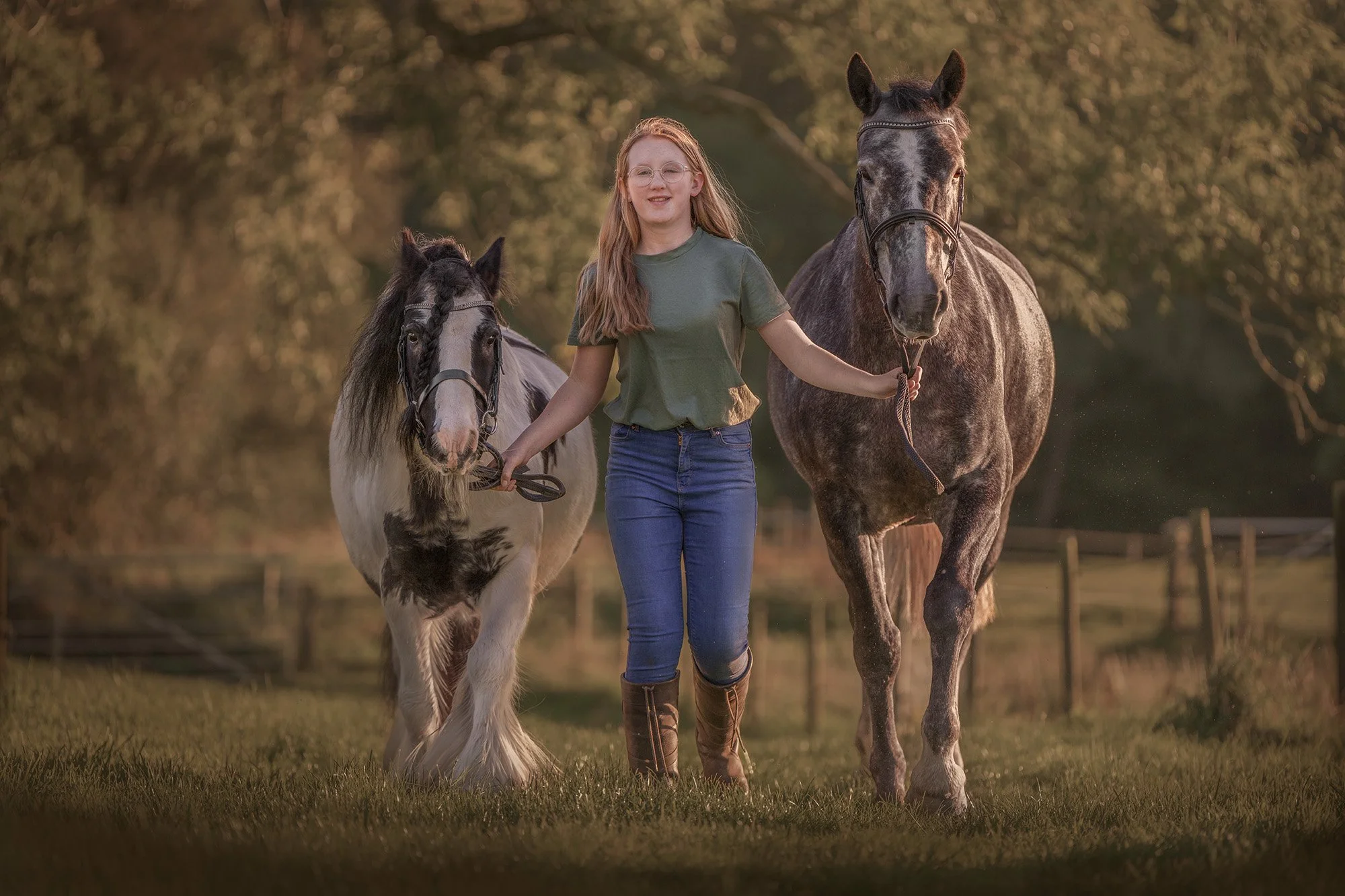 Teenage girl leads a copy pony and Irish Draught horse up a track, photographed in Cumbria by Frankie Adamson.