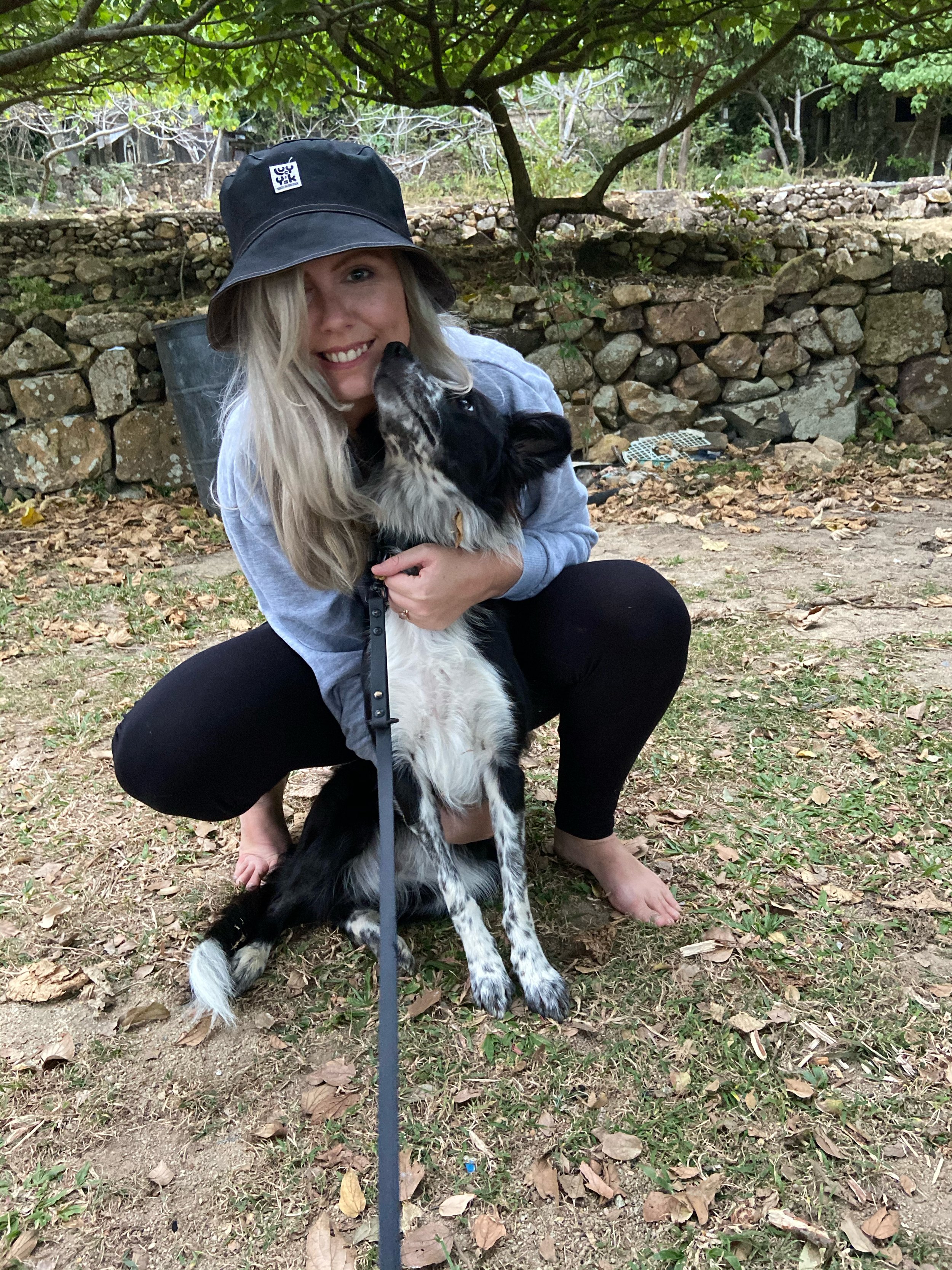 A woman crouching on the ground, holding and kissing a black and white Border Collie puppy.