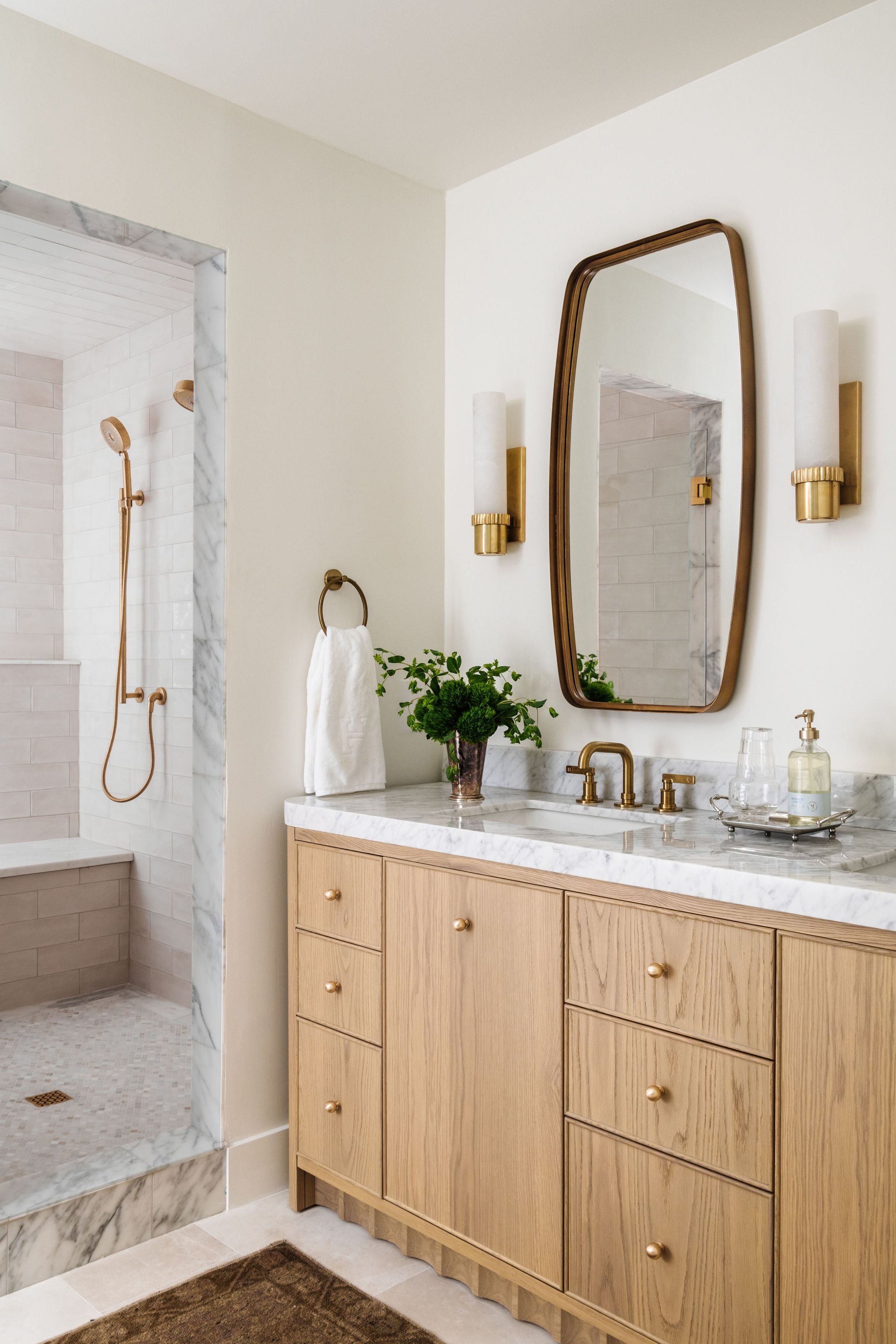 Bathroom with a vanity, mirror, and light fixtures. Shower area with marble tiles and a beige towel.