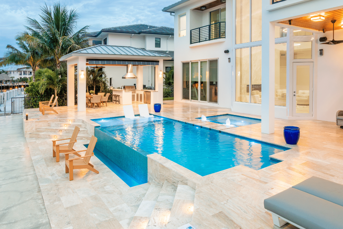 Luxury backyard with swimming pool, outdoor seating, and dining area at sunset, with large windows and sliding doors to the interior of the house