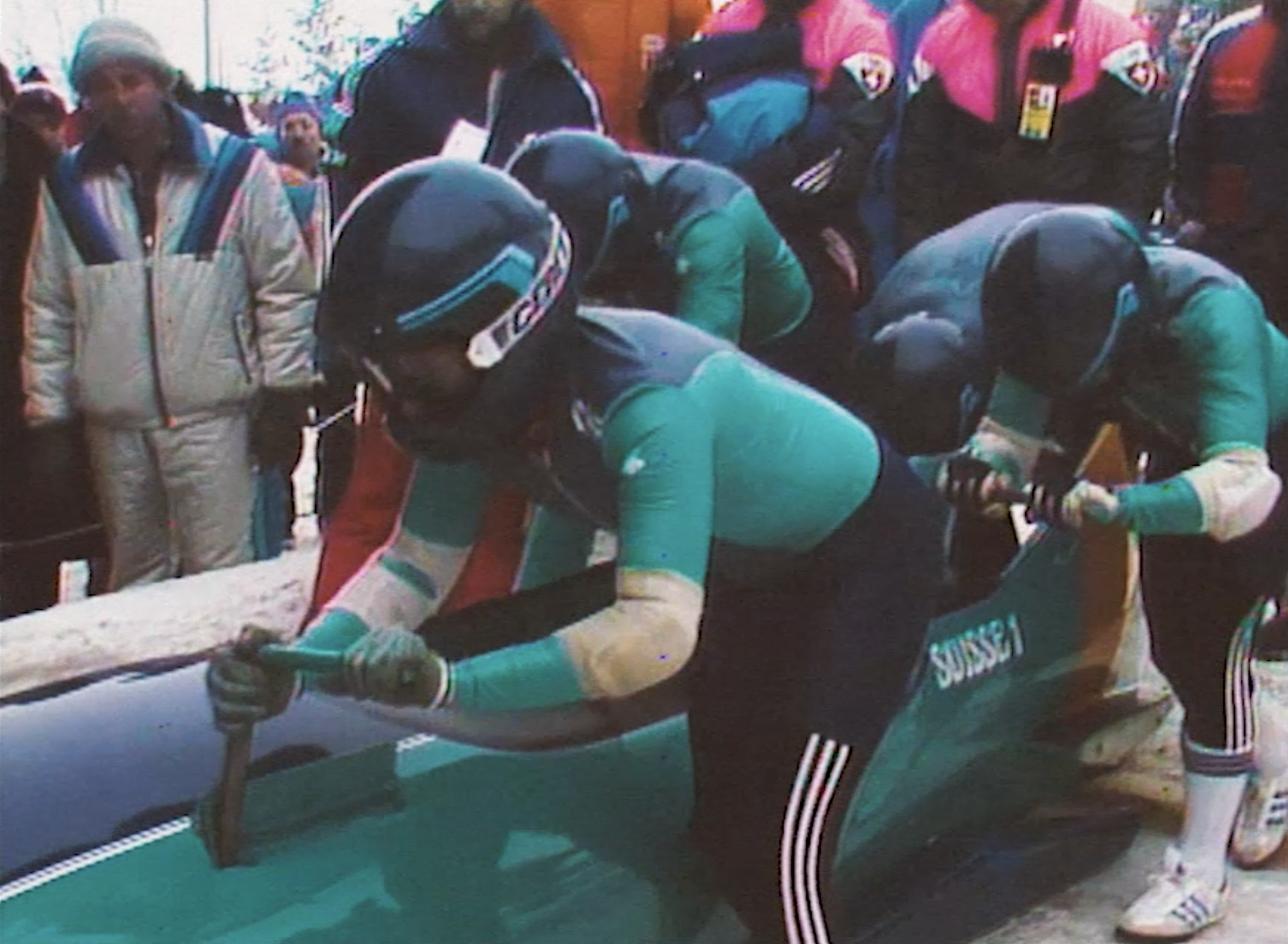 Des cyclistes en plein effort lors d'une compétition, portant des casques et des tenues de cyclisme colorées, avec un public spectateur derrière eux.