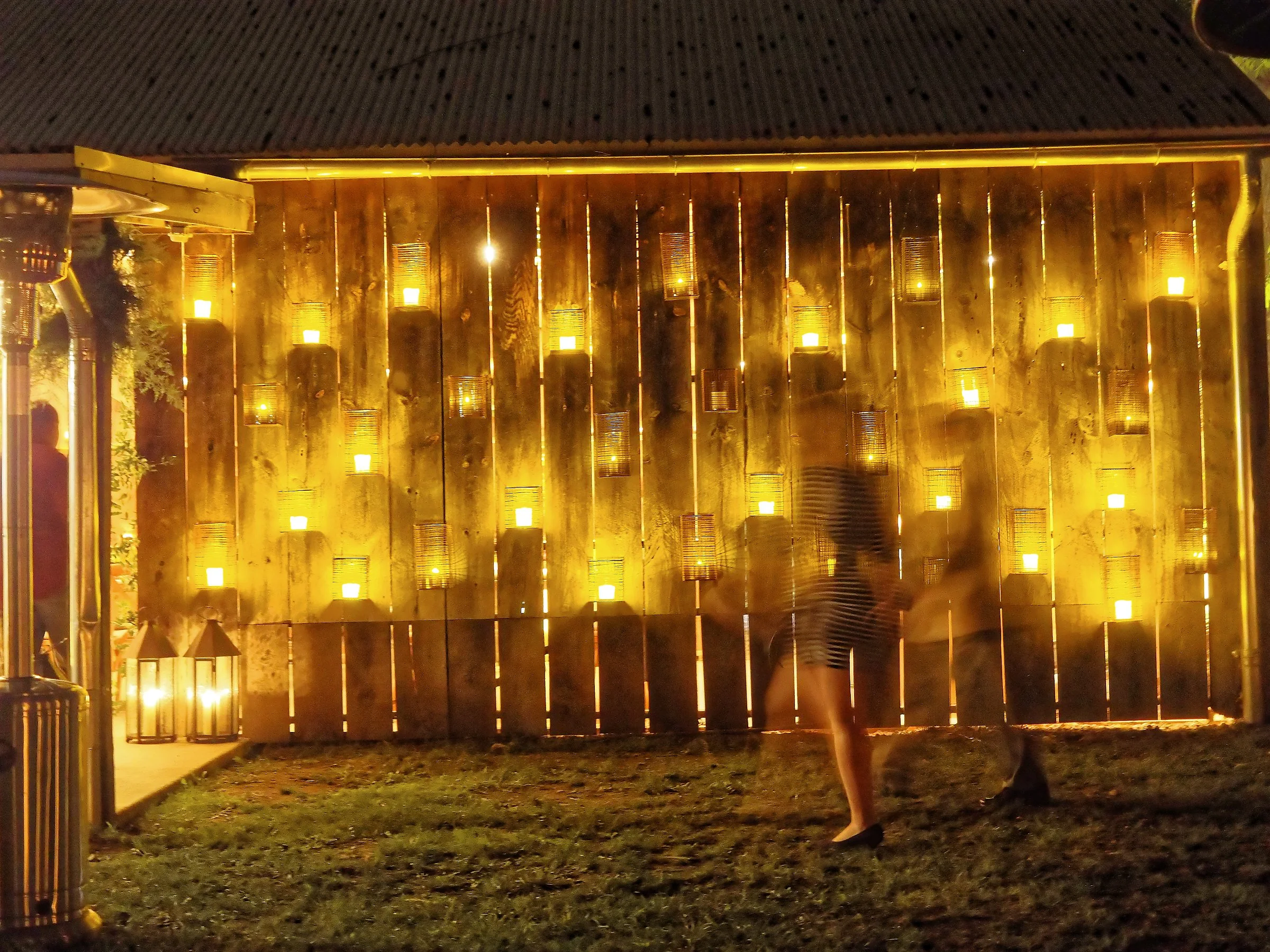 People dancing in front of a wooden wall with lights at night.